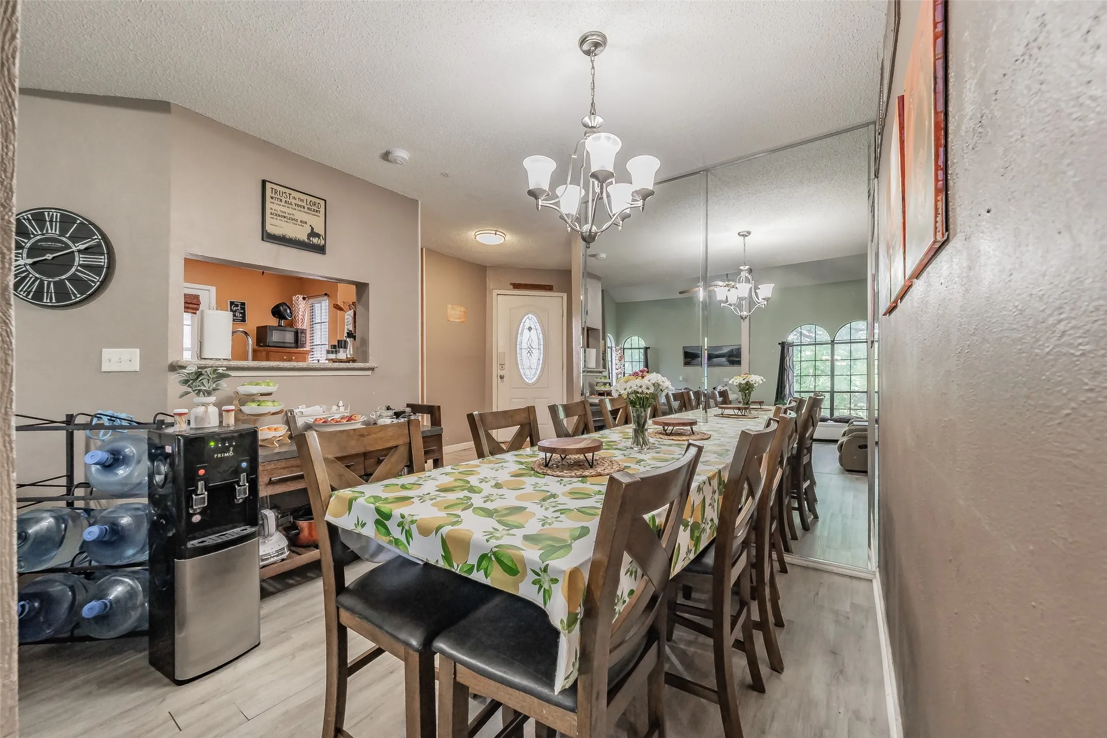 Open concept dining space featuring wood-finish flooring, a multi-light chandelier, a mirrored accent wall, a passthrough kitchen window, and an exterior door with decorative glass