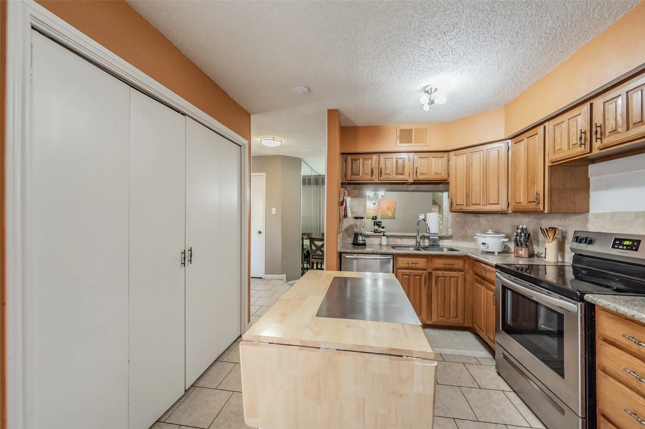 Kitchen featuring wood cabinetry, stainless steel appliances, tile flooring, and a central island with a wood-finish countertop