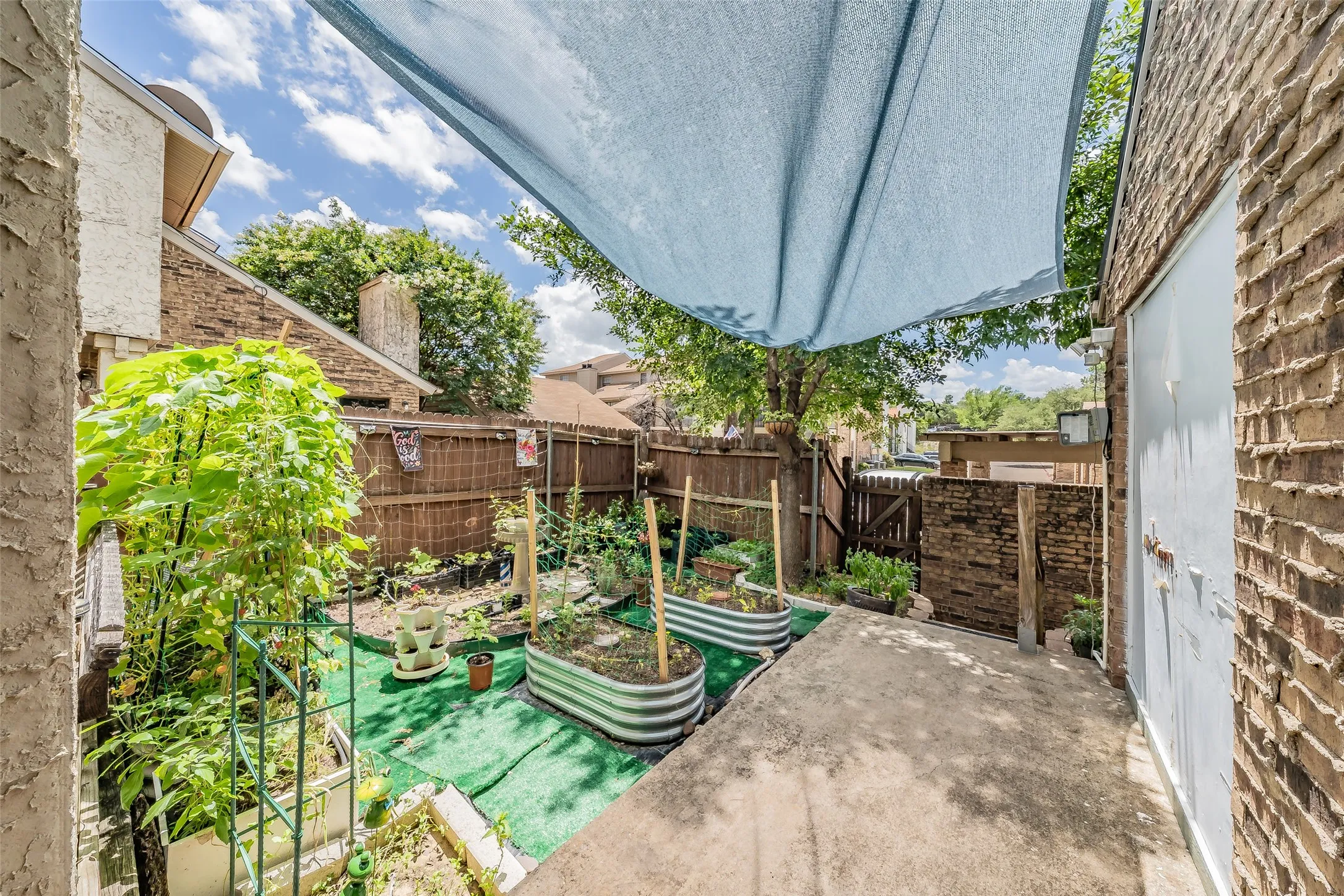 Private outdoor space featuring two raised garden beds, partial shade covering, and a concrete pathway