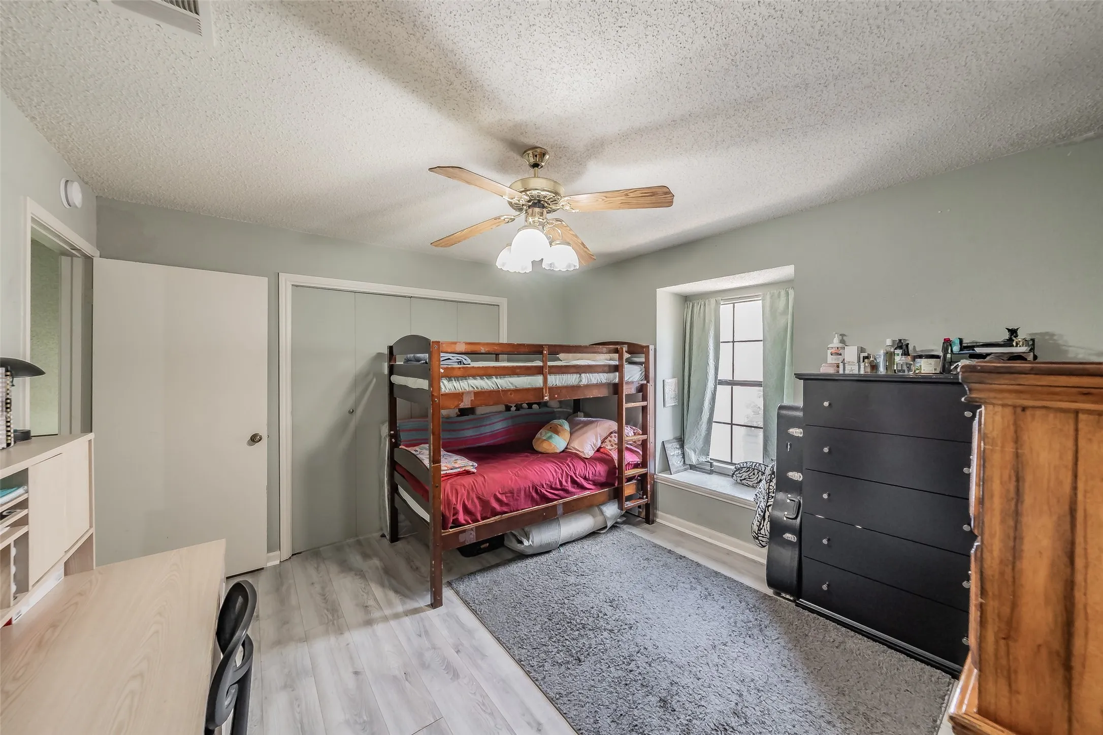 Bedroom featuring light-toned wood-finish flooring, a ceiling fan with integrated lighting, a built-in window bench, a window with natural light, and sliding closet doors