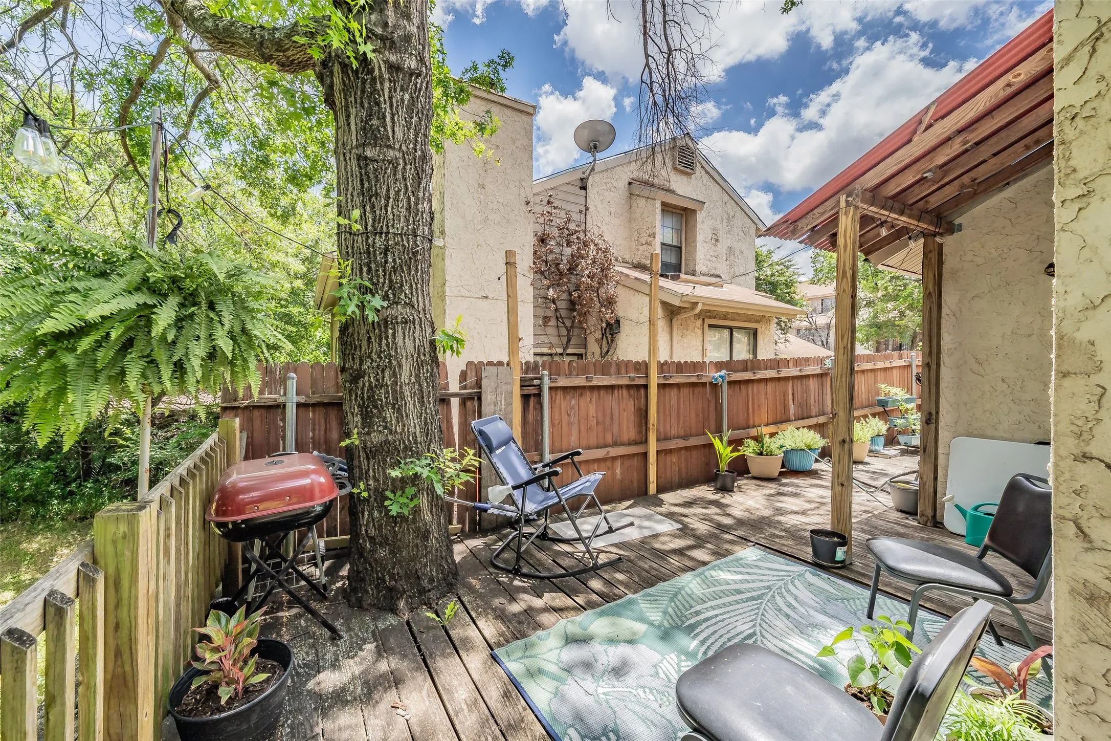 Spacious outdoor deck area featuring wood decking, a privacy fence, and mature trees