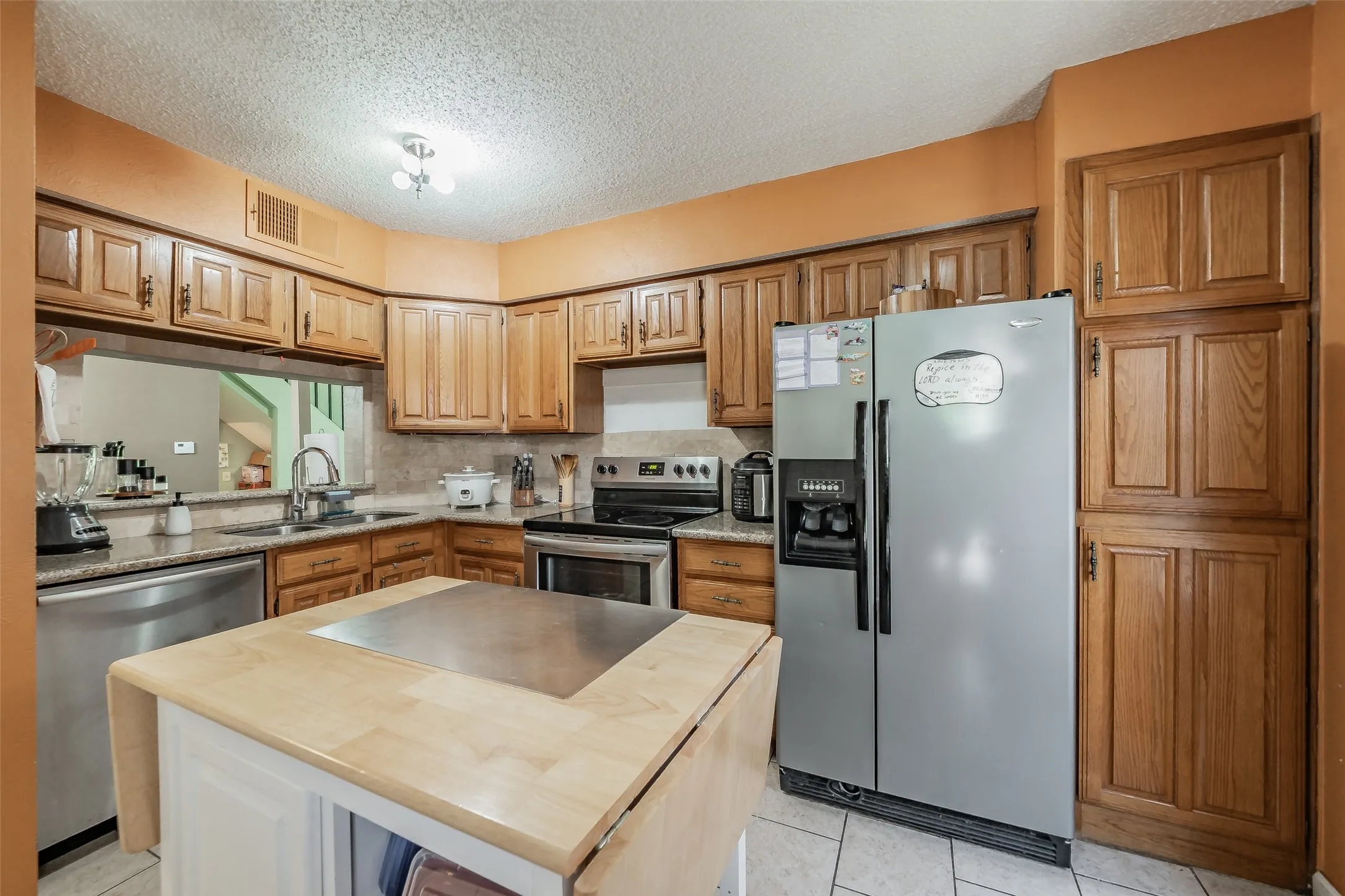 Kitchen featuring wood cabinetry, stainless steel appliances, a pass-through window, and a central island with a drop-leaf extension