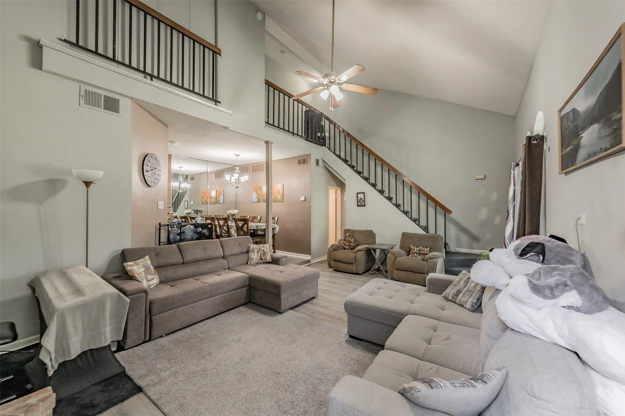 Vaulted ceilings with a ceiling fan, exposed staircase with black metal balusters and wood-finish handrails, and wood-finish flooring