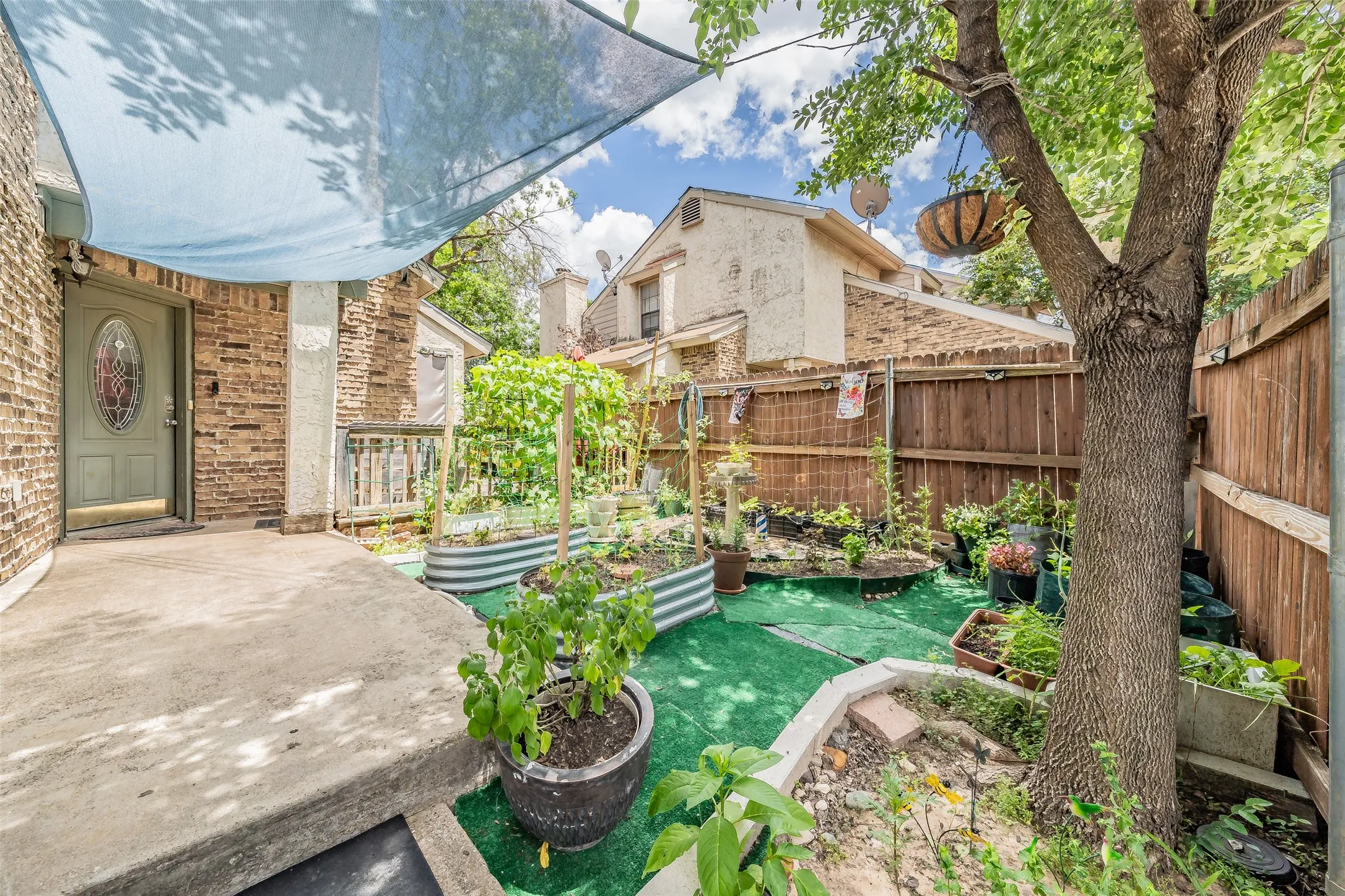 Private outdoor space featuring a covered patio with concrete flooring, raised garden beds, and mature trees providing natural shade