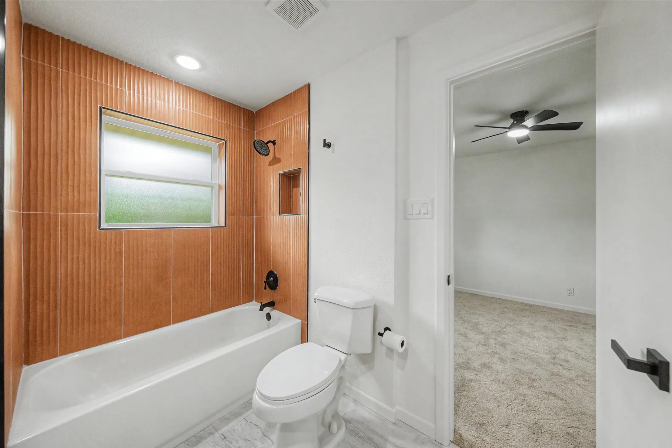 Bathroom featuring a white tub, textured tile surround, and matte black fixtures