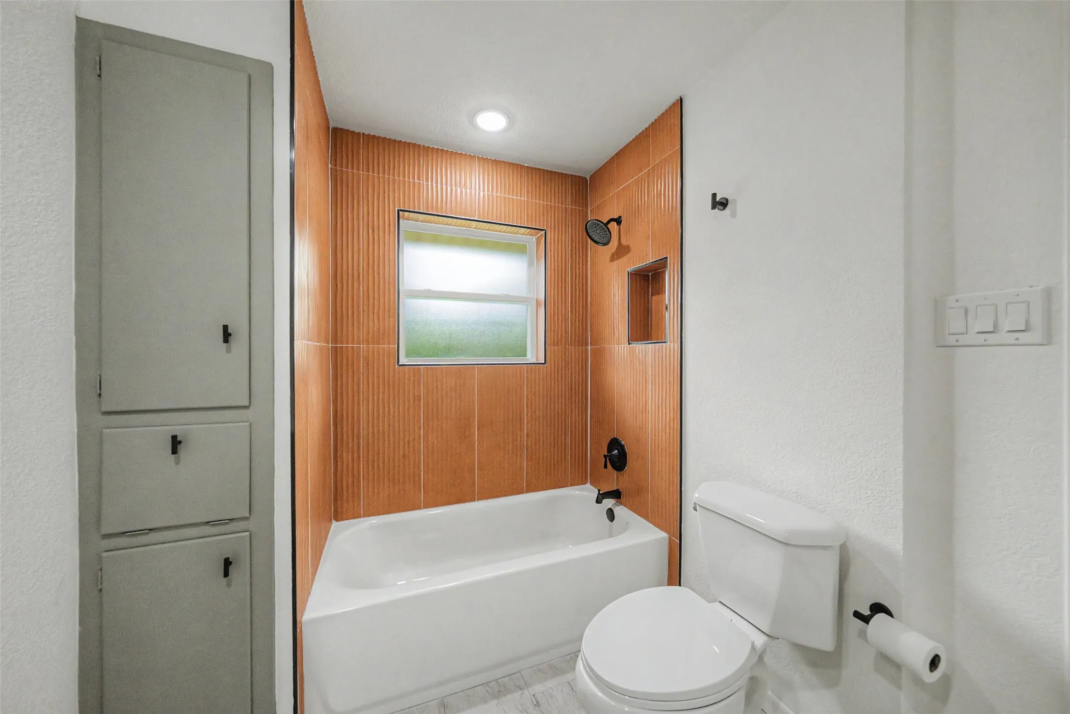 Bathroom featuring a white bathtub, toilet, and built-in vertical storage