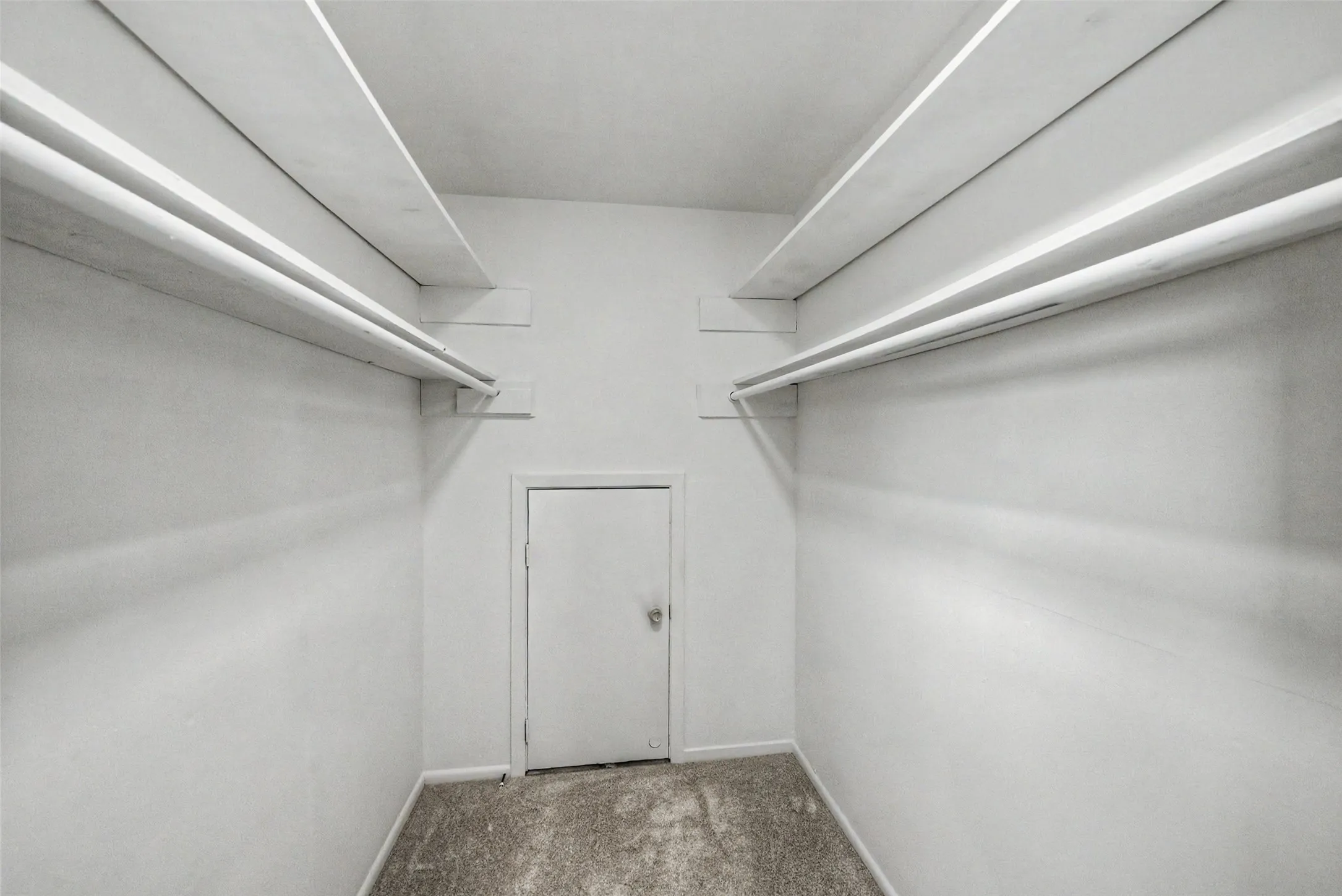 Walk-in closet featuring white walls, textured carpeting, and double hanging rods with upper shelving on opposing sides