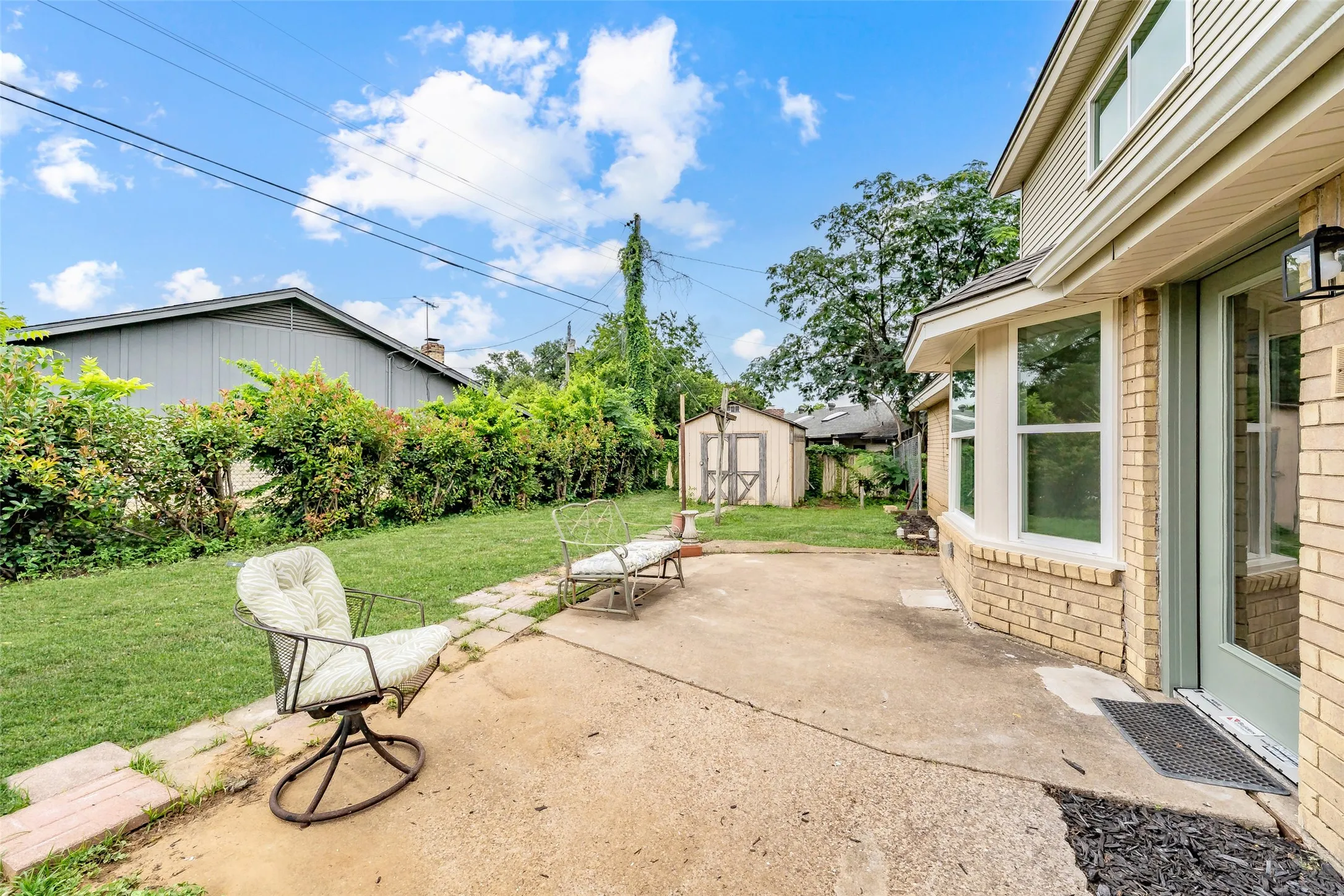 Expansive backyard featuring a concrete patio, mature green lawn, and shrubbery