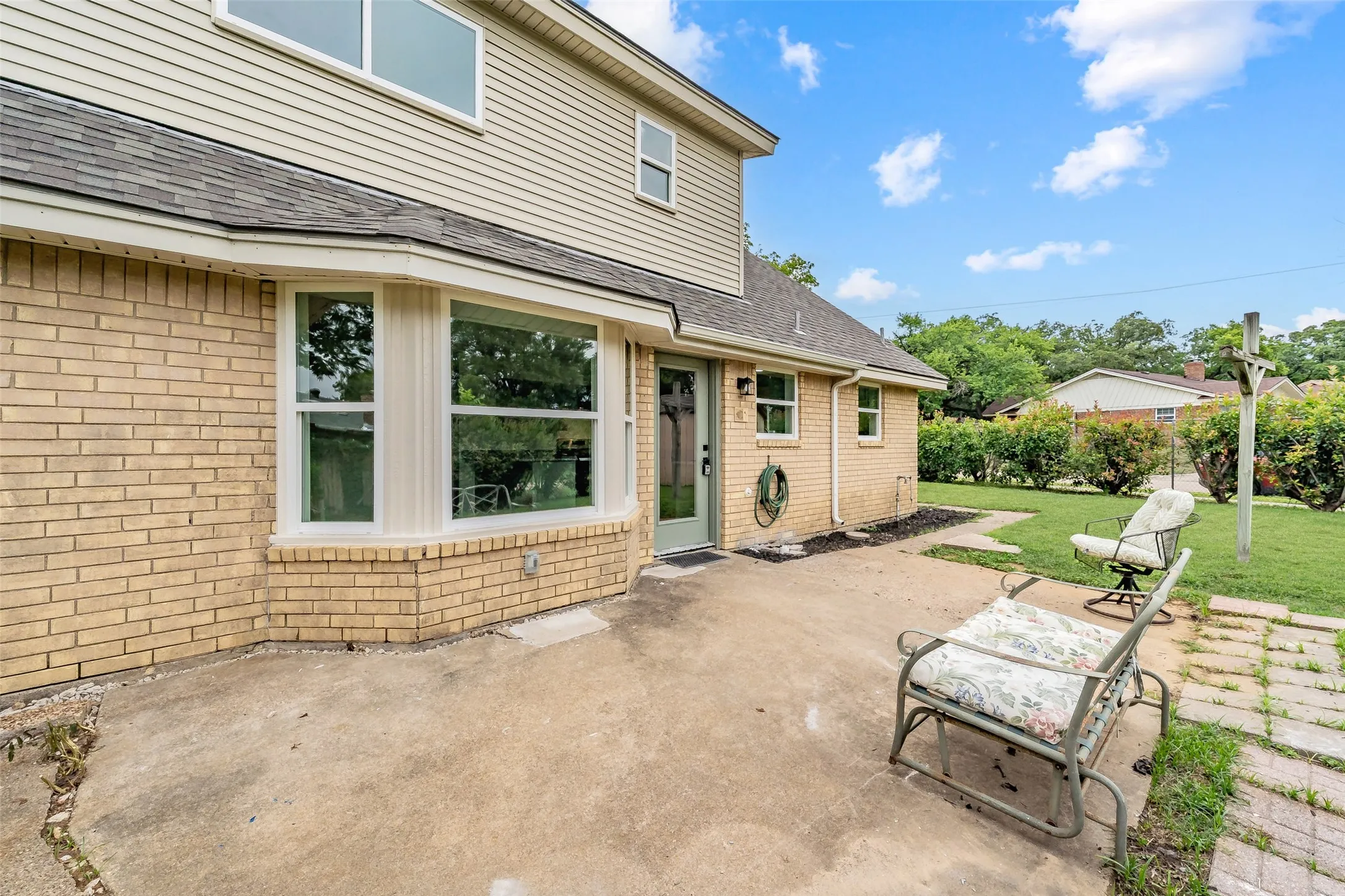Rear exterior featuring a concrete patio, light brick facade, and a bay window