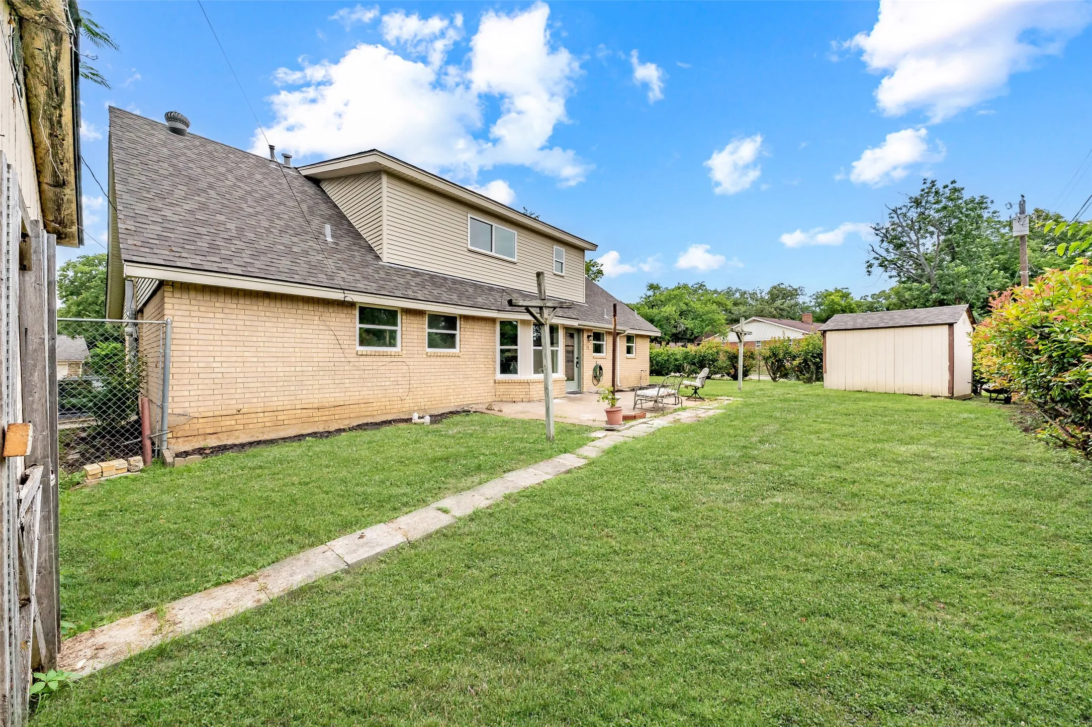 Expansive lawn area with a concrete patio, perimeter fencing, and a detached storage shed