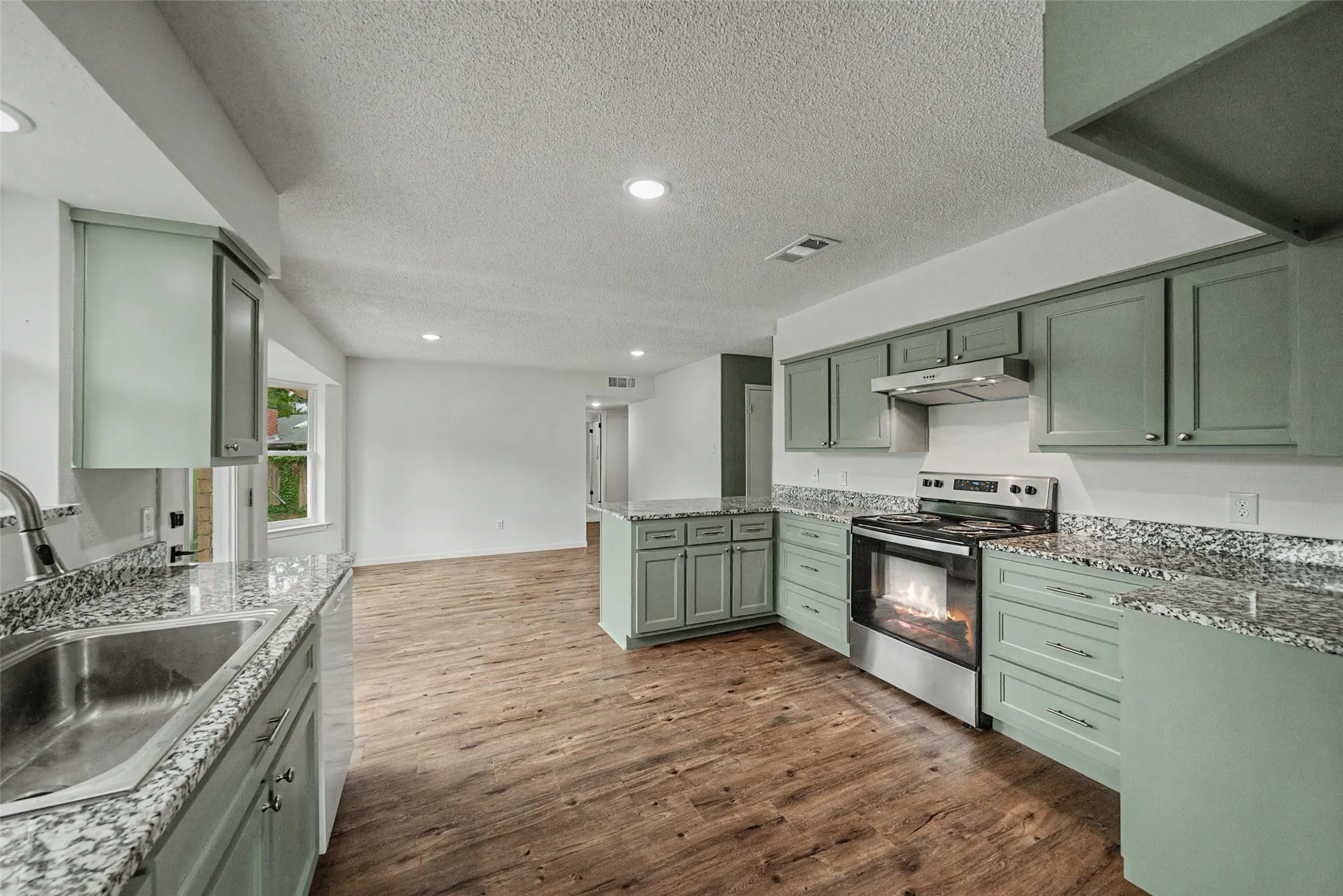 Modern kitchen featuring light green cabinetry, stainless steel appliances, granite countertops, and wood-finish flooring