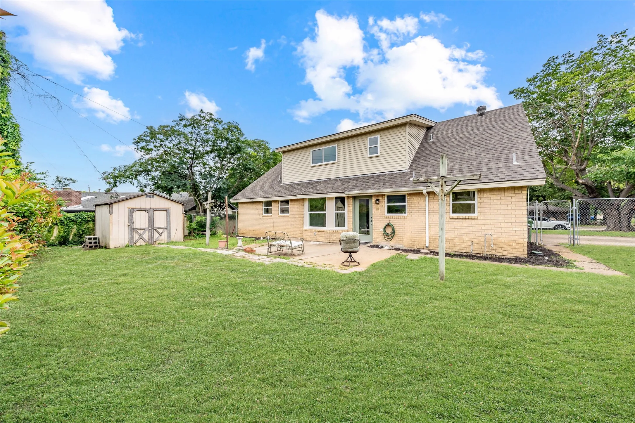 Spacious backyard featuring a large grassy area, a detached storage shed, a paved patio, and a light brick exterior with siding on the upper level