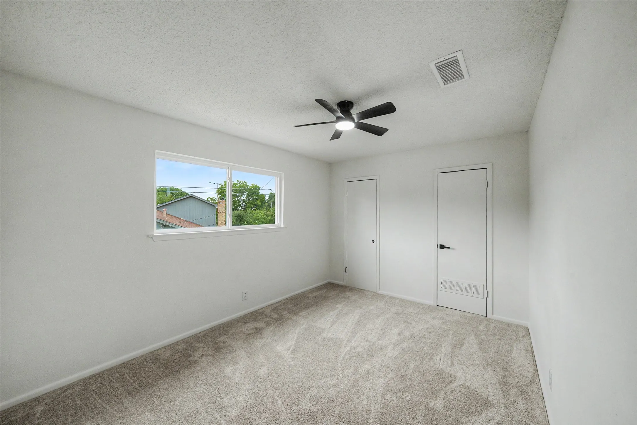 Bright interior room featuring neutral-toned carpet flooring, white walls, and a large window