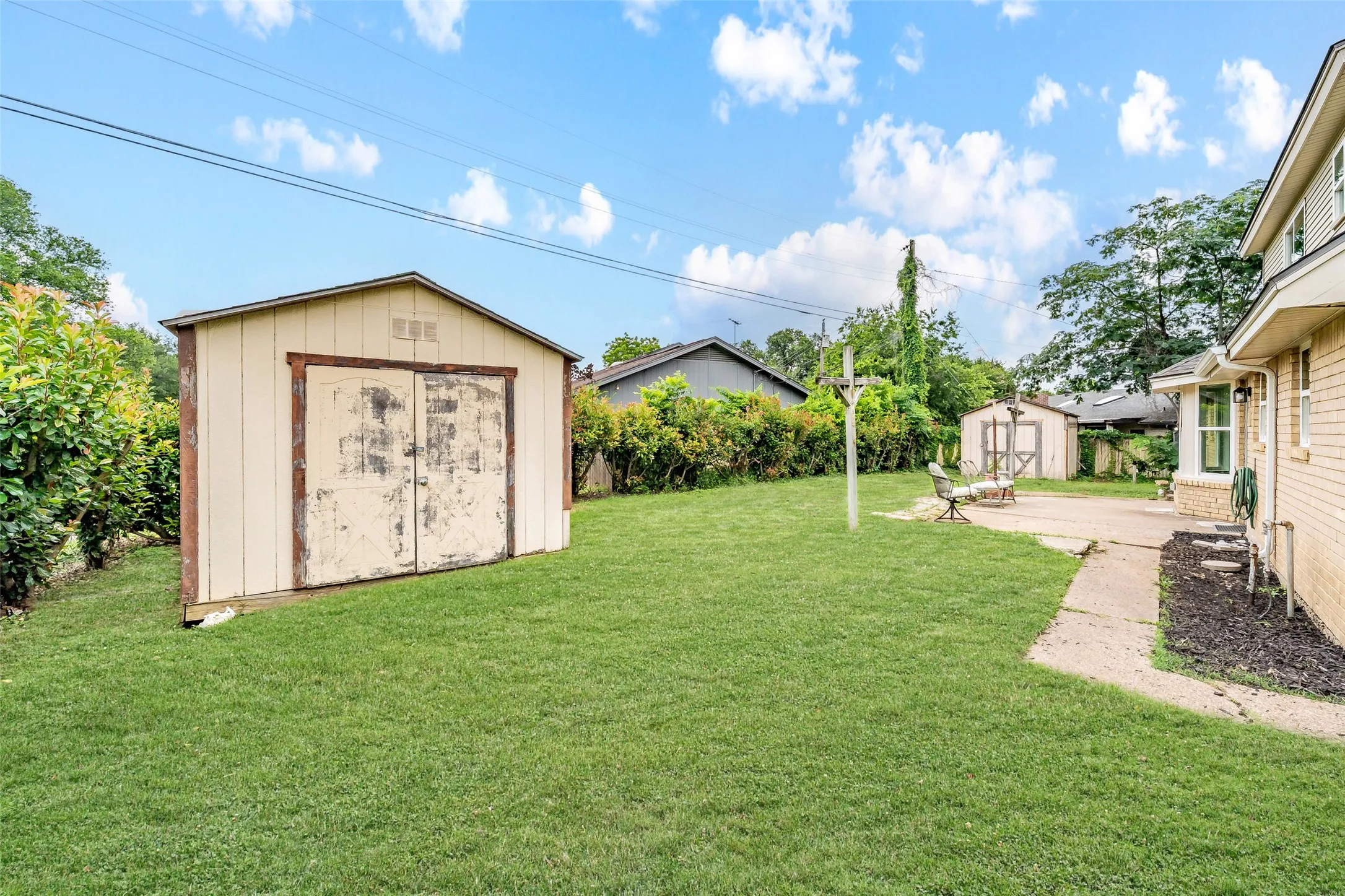 Expansive rear yard featuring a detached storage shed, a concrete patio, and a second storage shed in the background