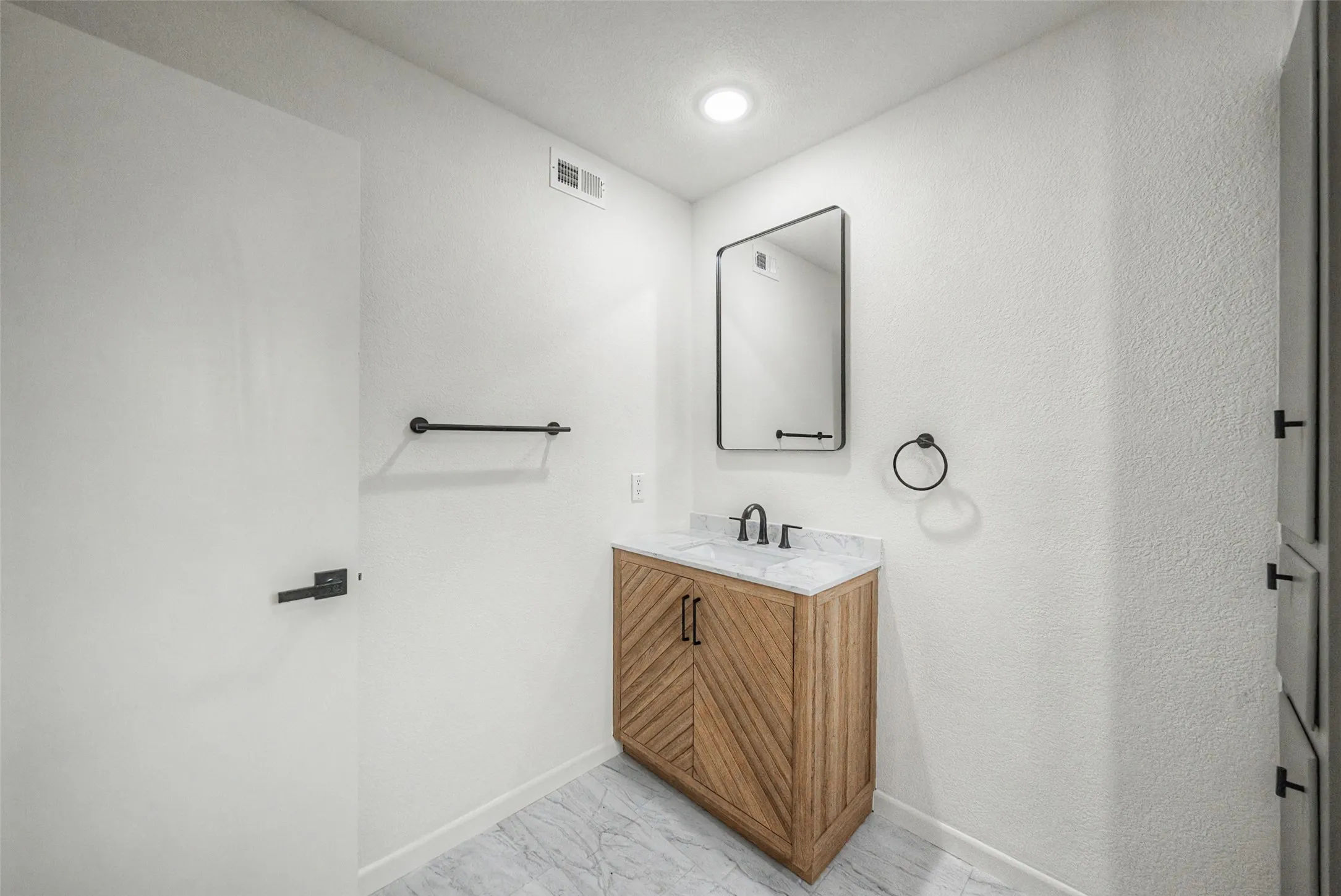 Bathroom vanity featuring a wood-finish cabinet with chevron paneling, a white countertop with gray veining, and a black-framed rectangular mirror