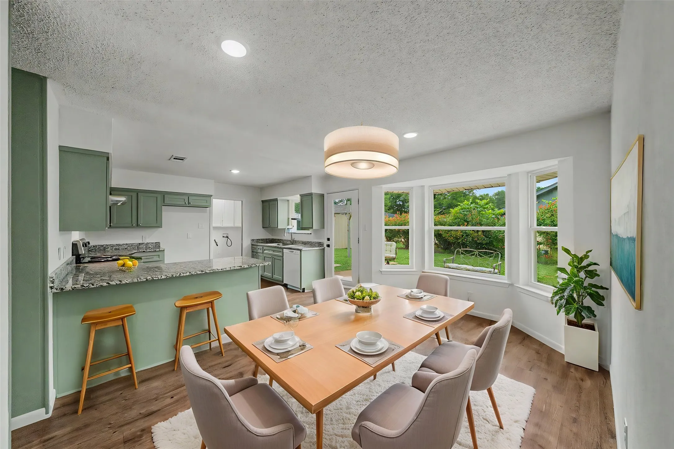 Open-concept dining area featuring wood-finish flooring, a contemporary chandelier, and a bright bay window overlooking the rear yard