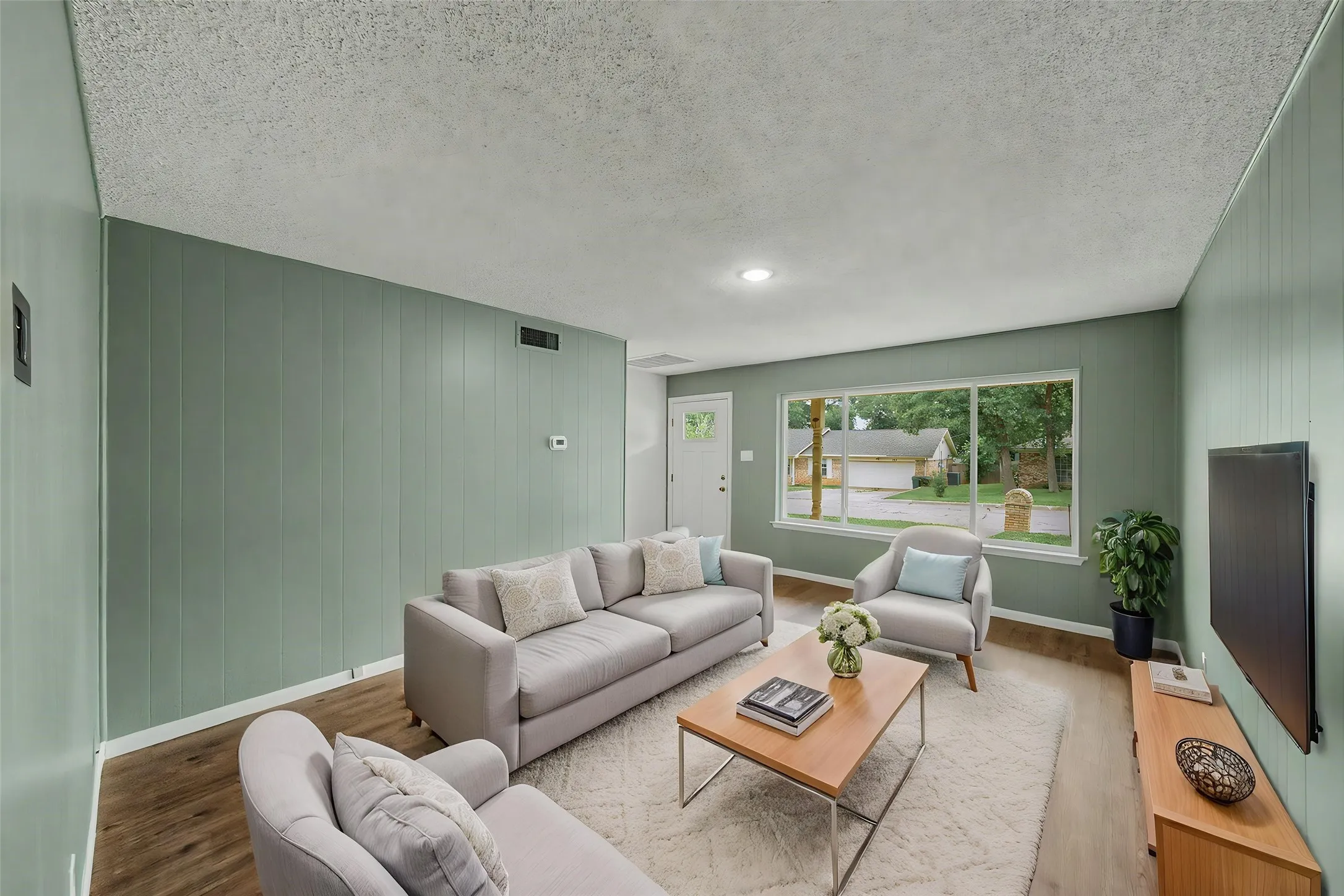 Living area featuring wood-finish flooring, recessed lighting, a large picture window, and paneled walls