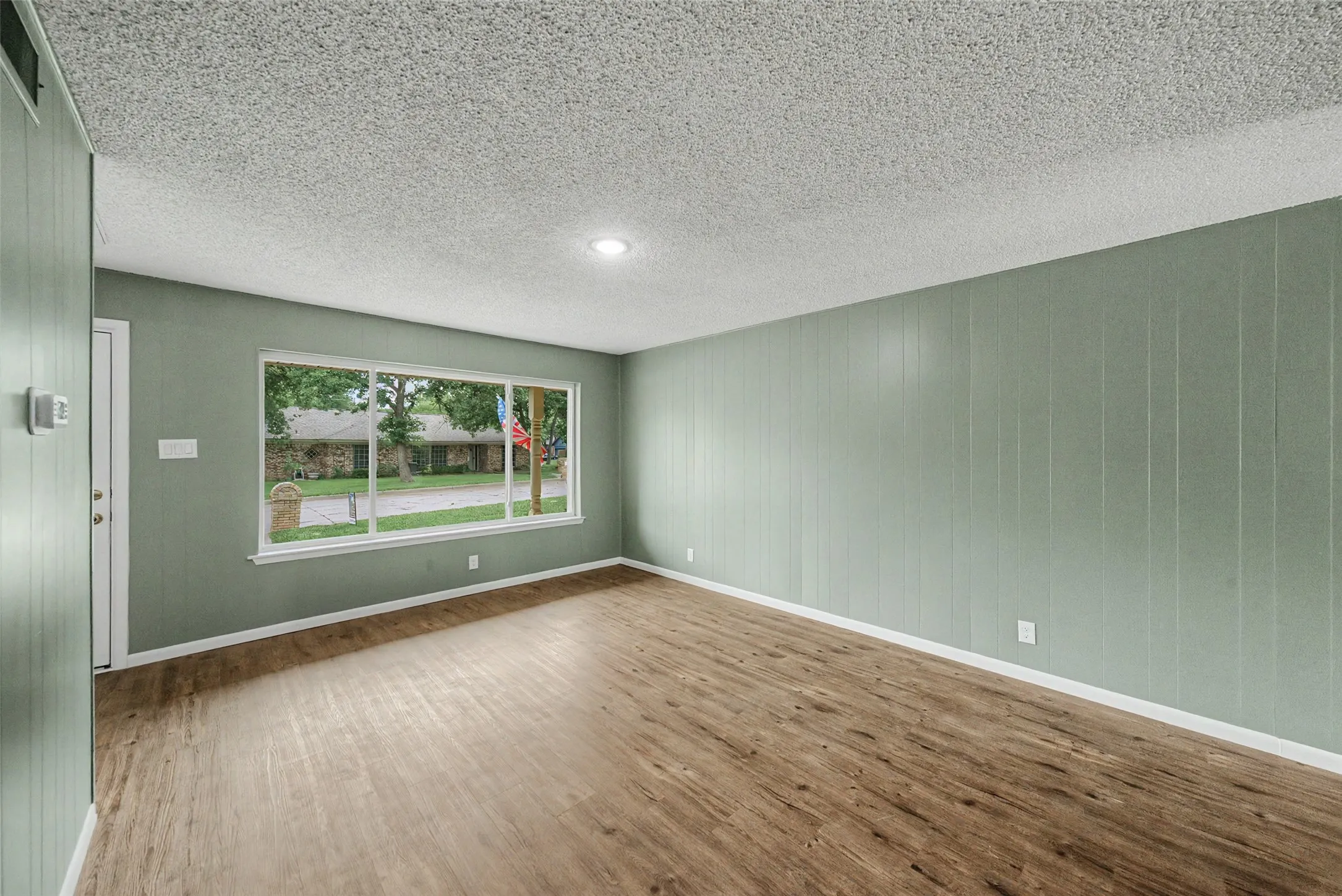 Spacious room featuring wood-finish flooring, light green paneled walls, and a large multi-pane window