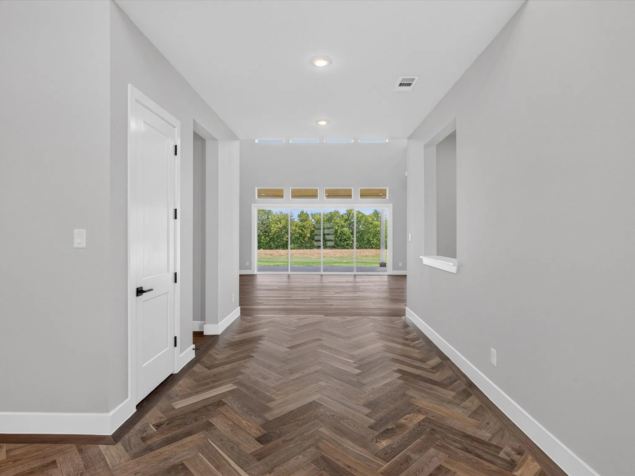 Herringbone-pattern wood-finish flooring, recessed lighting, and white interior doors with black hardware