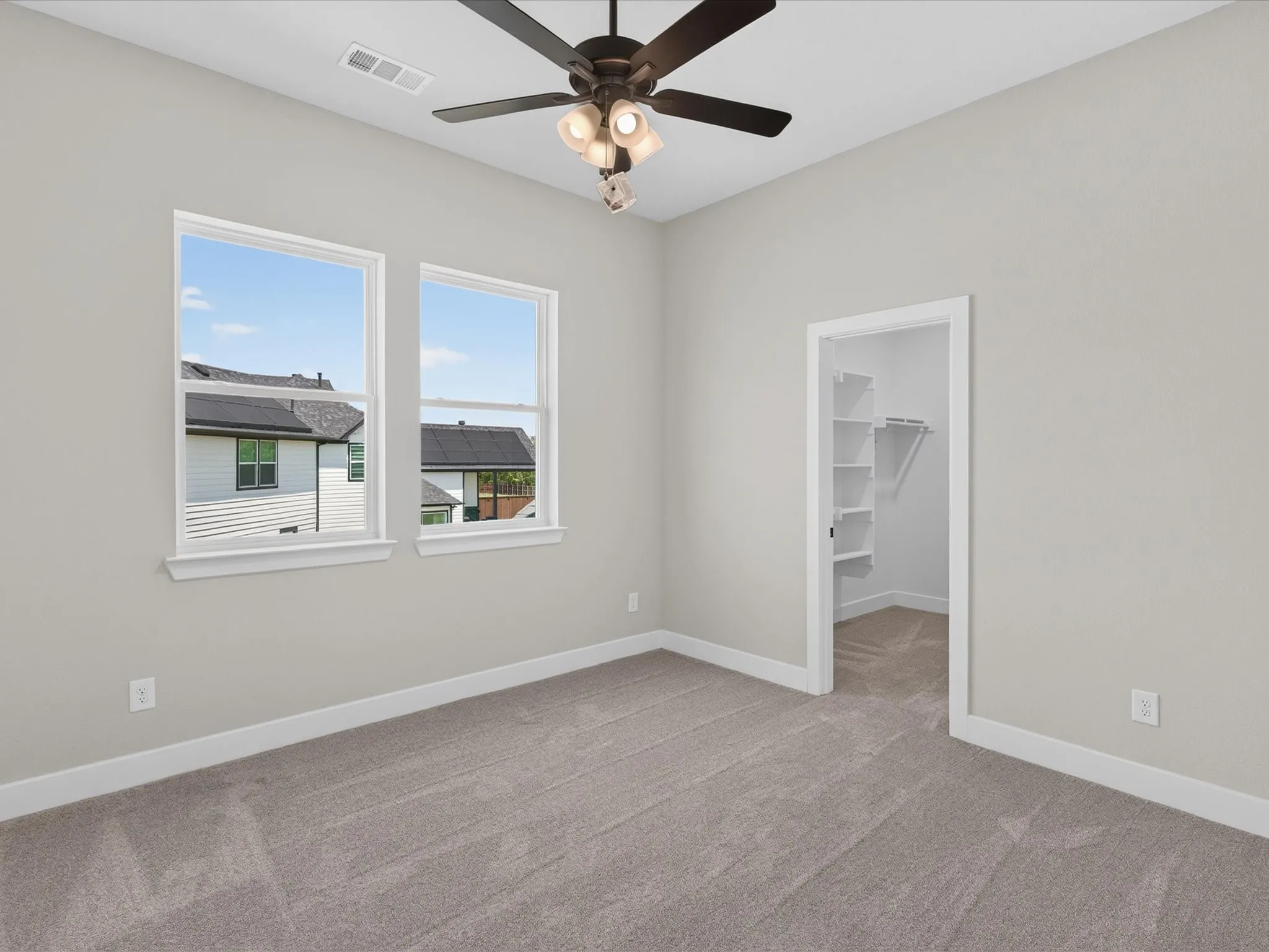 Carpeted room featuring multiple windows, a ceiling fan with light fixture, and an open doorway leading to a closet with built-in shelving