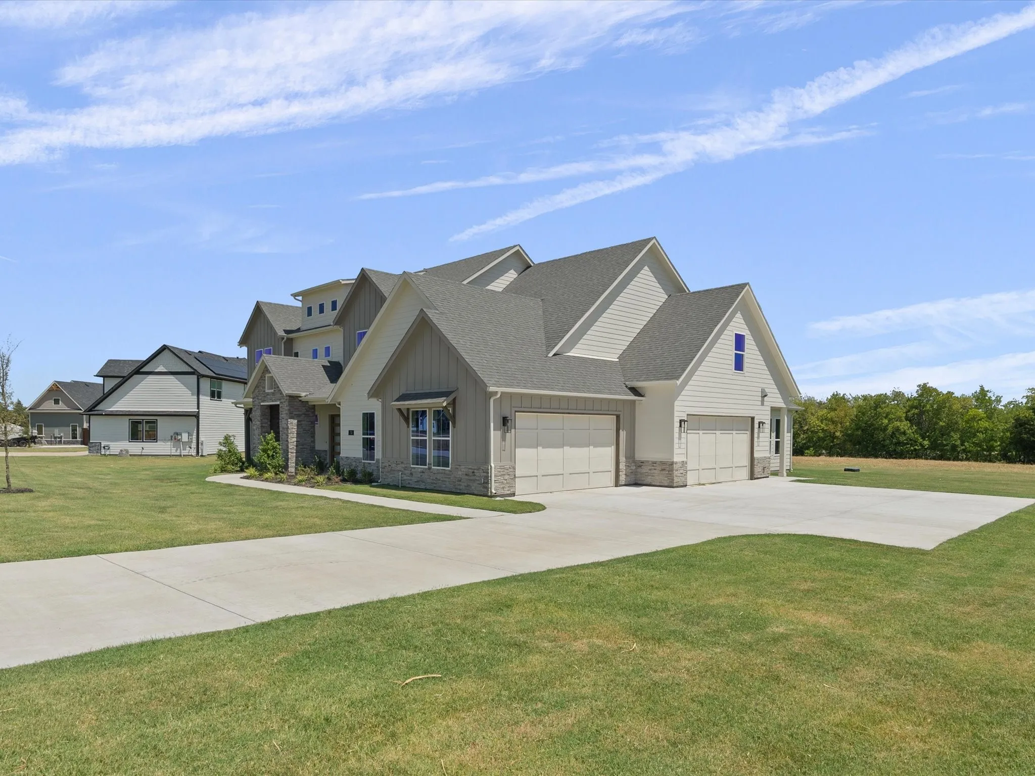 Gable rooflines with gray shingles, stone accent facade, white siding, and an attached two-car garage