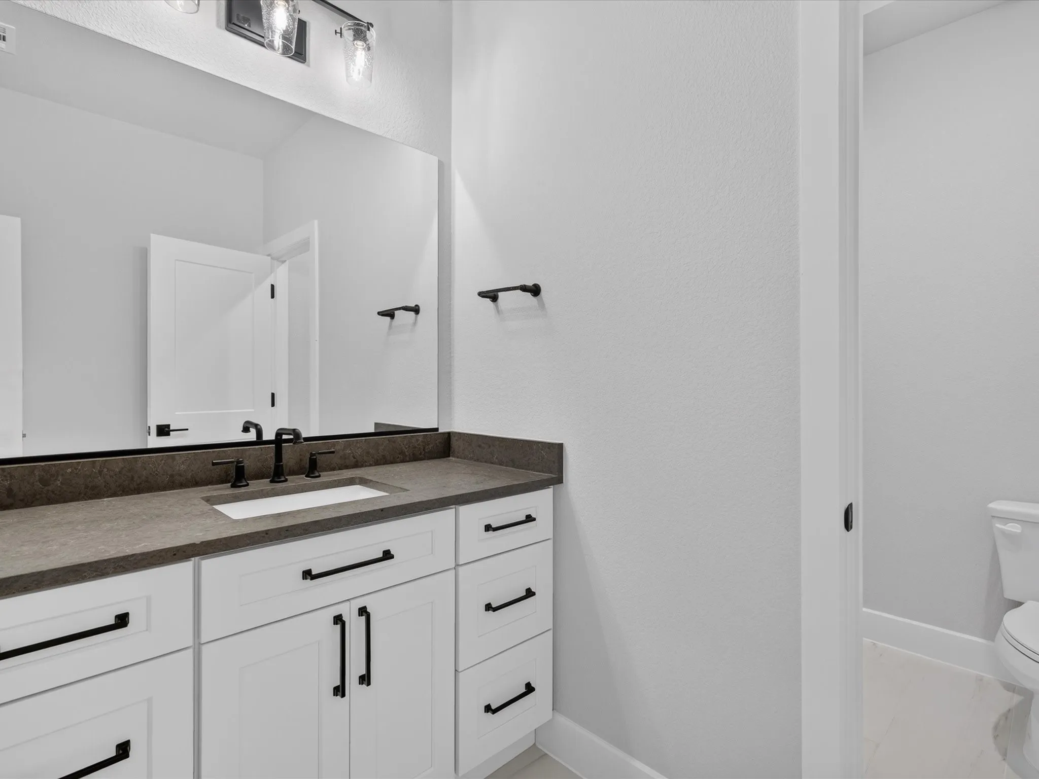 White cabinetry with matte black hardware, dark countertop, rectangular undermount sink, matte black faucet, and a large wall-mounted mirror