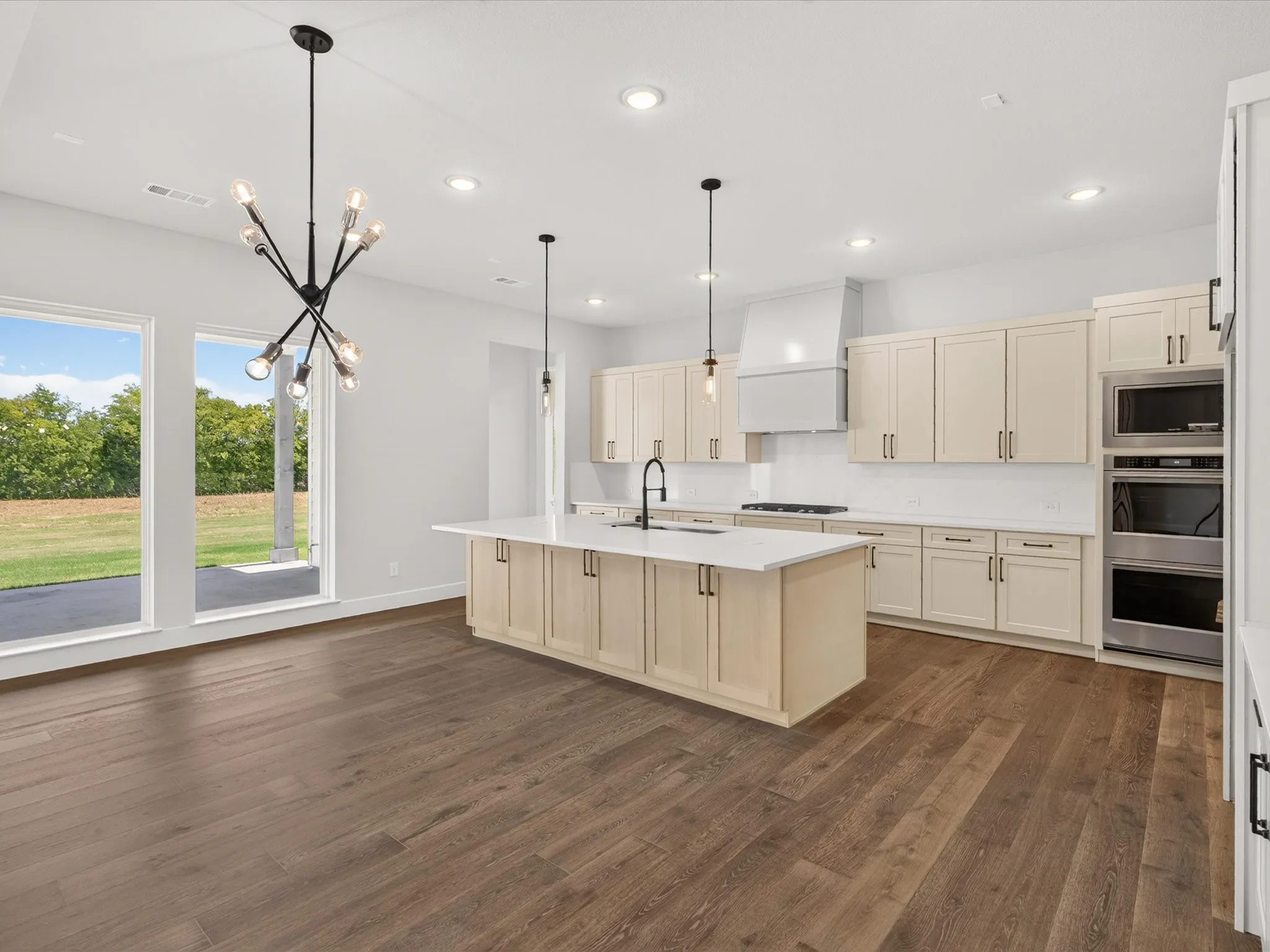 Wood-finish flooring, full-height cabinetry, kitchen island with sink, stainless steel appliances, and large windows