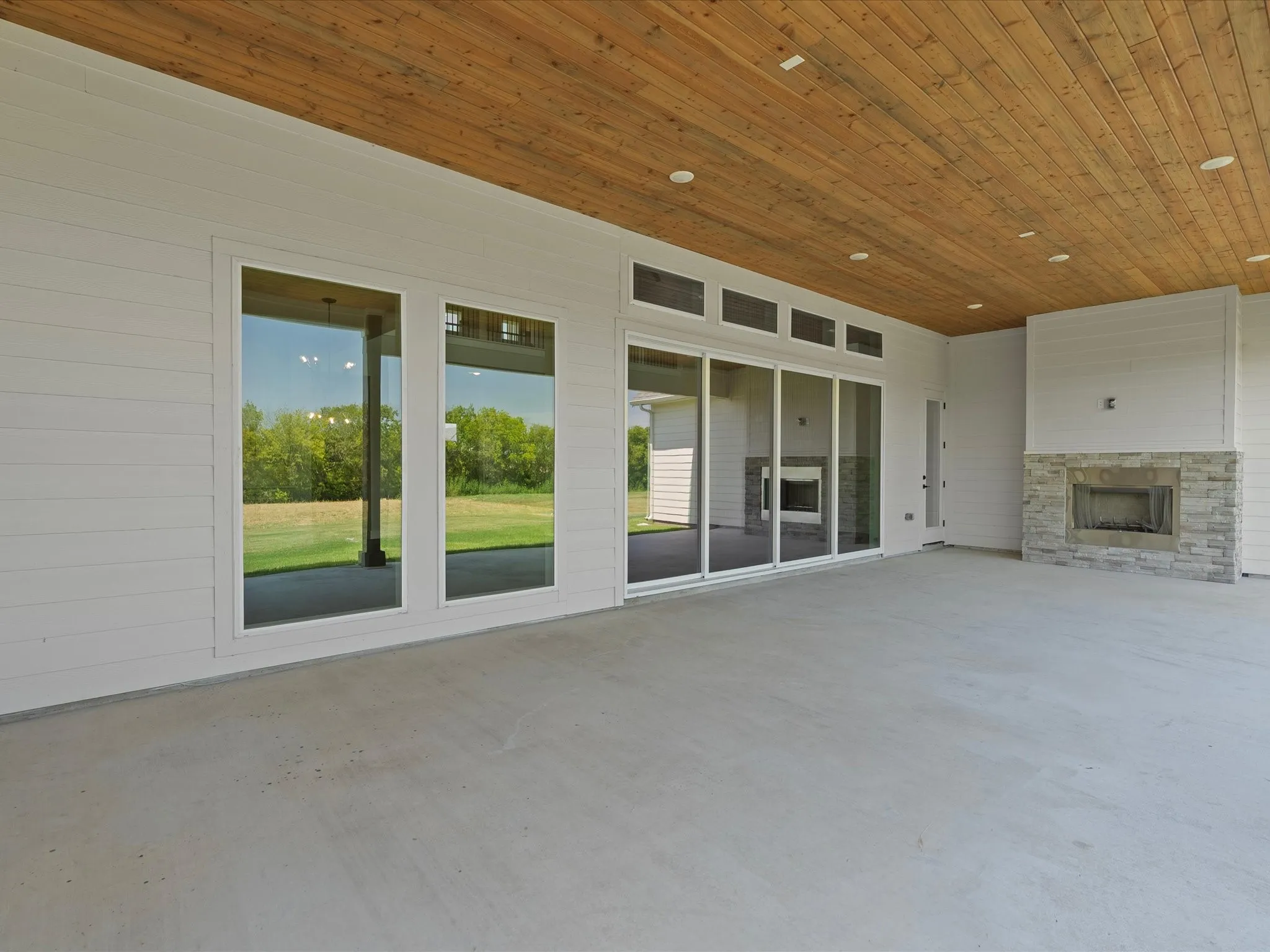 Expansive covered patio featuring a wood-panel ceiling, recessed lighting, and a stone-clad fireplace