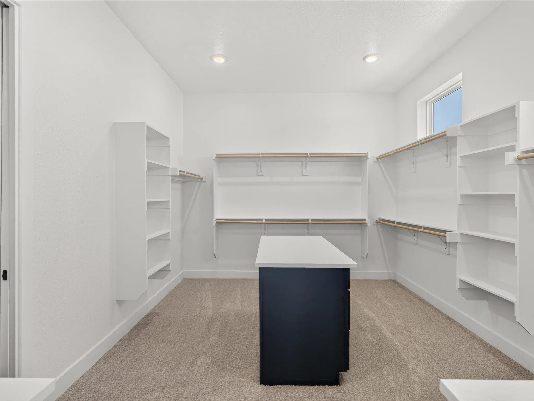 Walk-in closet featuring carpet flooring, built-in shelving, an opaque window, recessed lighting, and a central island with a light-toned countertop