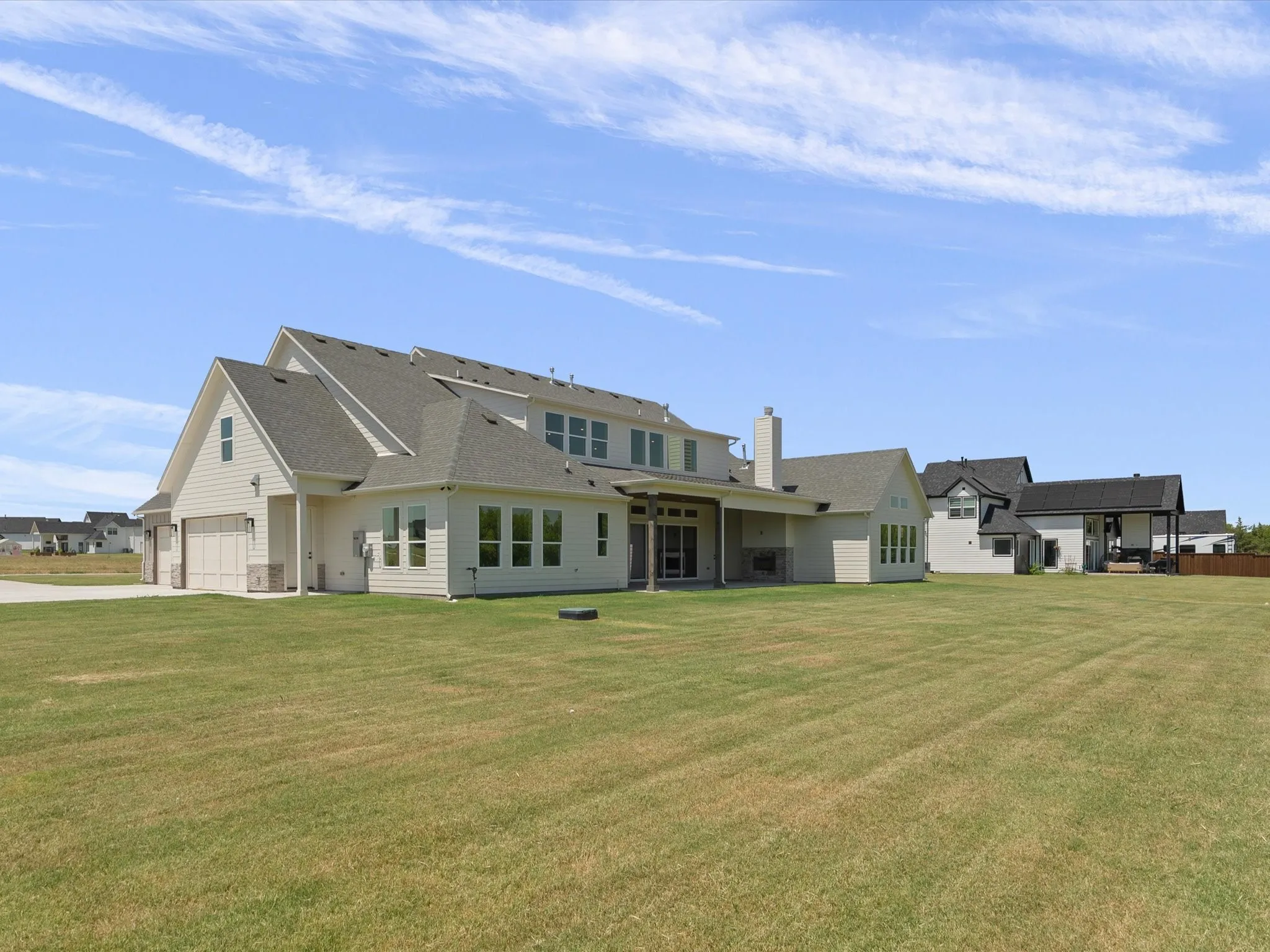 Expansive backyard with manicured lawn, multi-story exterior with light-colored siding, covered patio, multiple windows, and attached garage