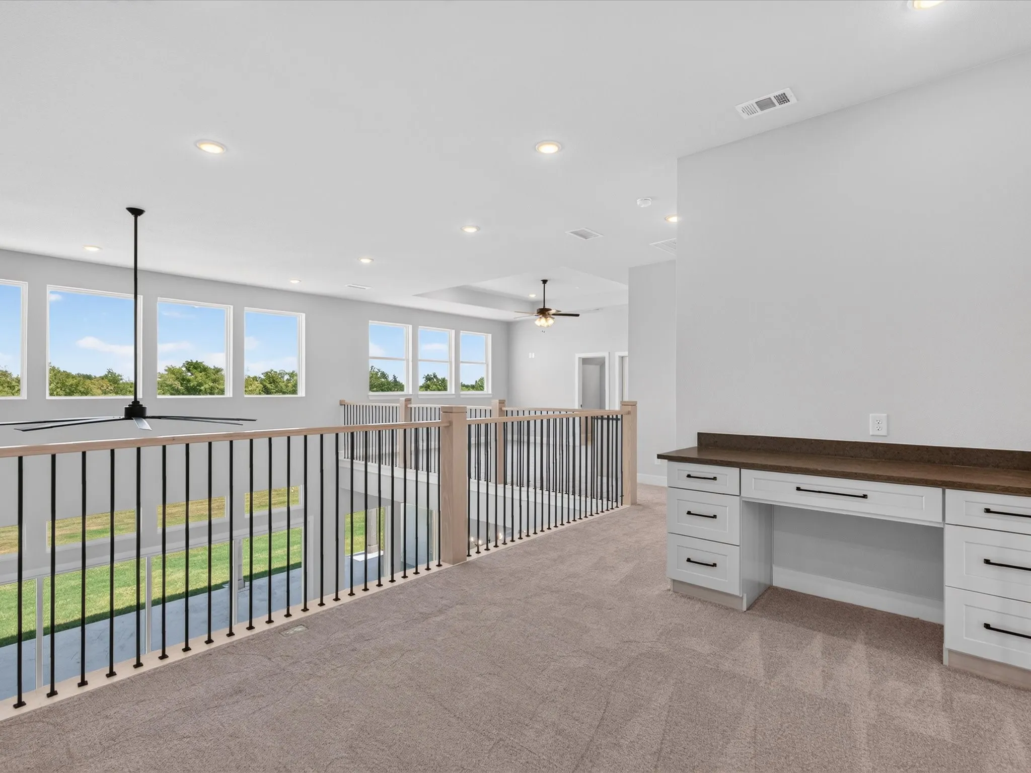Loft space featuring neutral carpeting, a built-in desk with white cabinetry and dark hardware, recessed lighting, and multiple windows