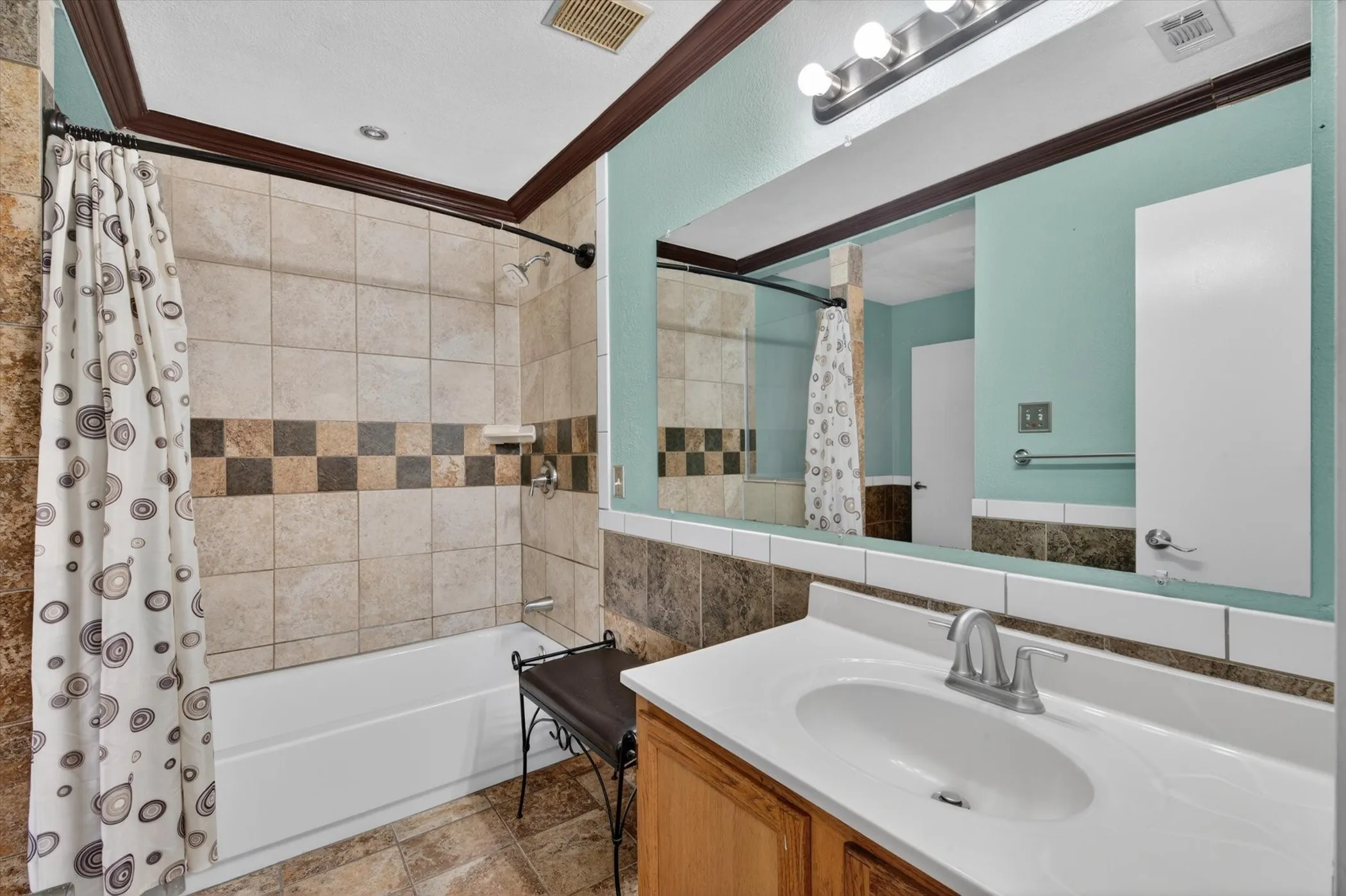 Bathroom featuring a white bathtub, tiled shower surround with accent band, vanity with integrated sink, and a large wall-mounted mirror