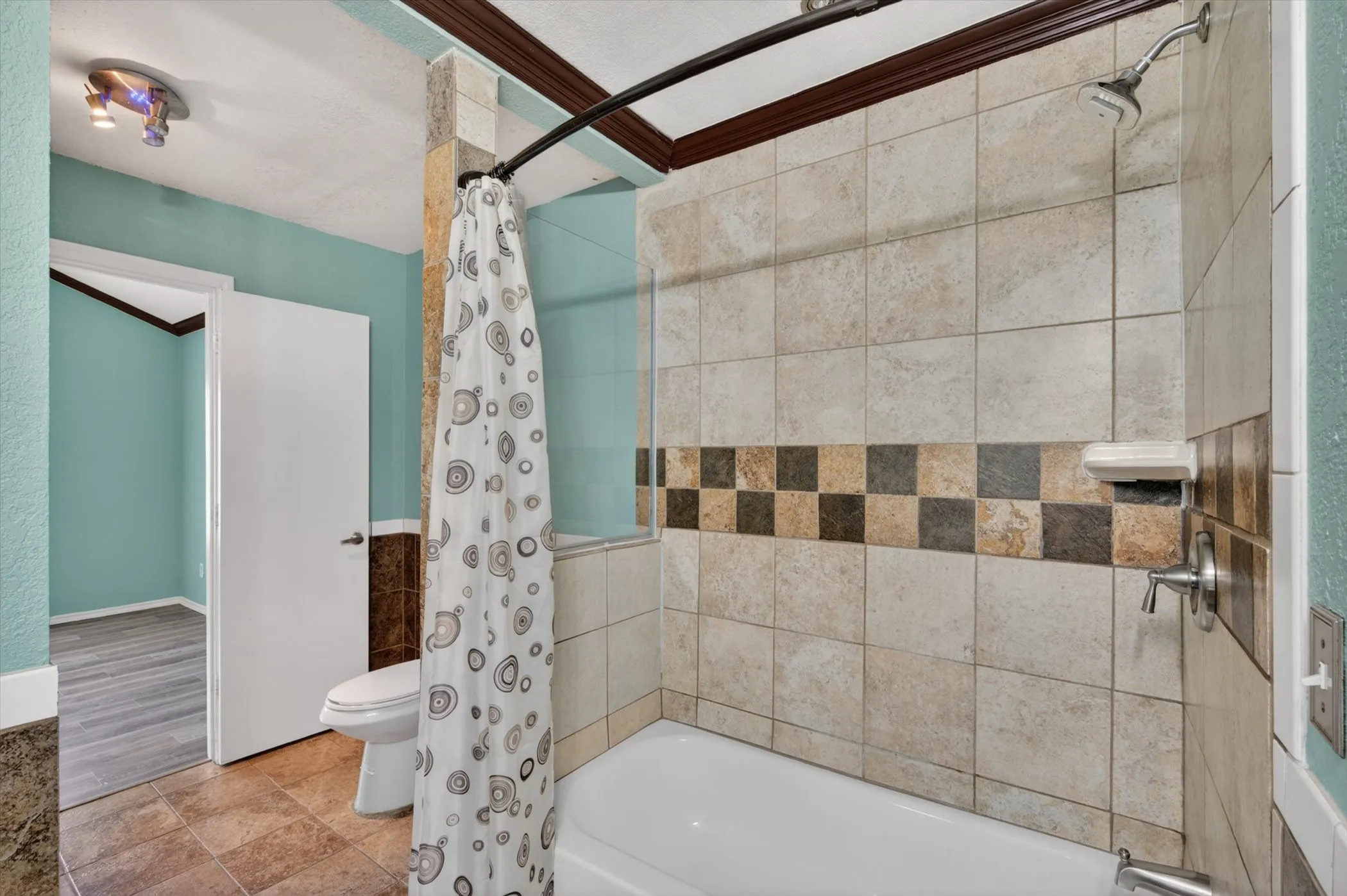 Bathroom featuring a shower-tub combination with light-toned wall tiling and a decorative mosaic accent band