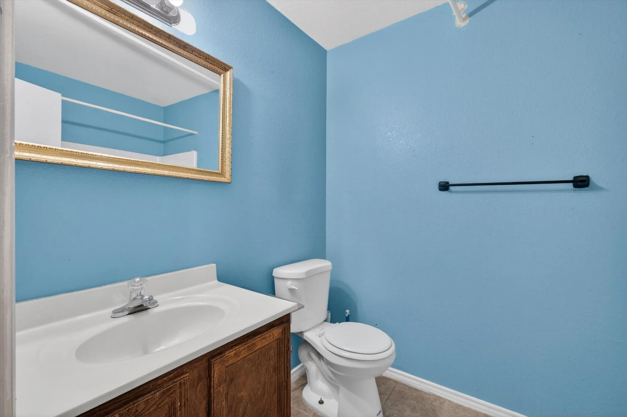 Powder room featuring a wood-finish vanity with a white countertop and integrated sink, a frameless mirror with a gold-tone frame, and a white toilet