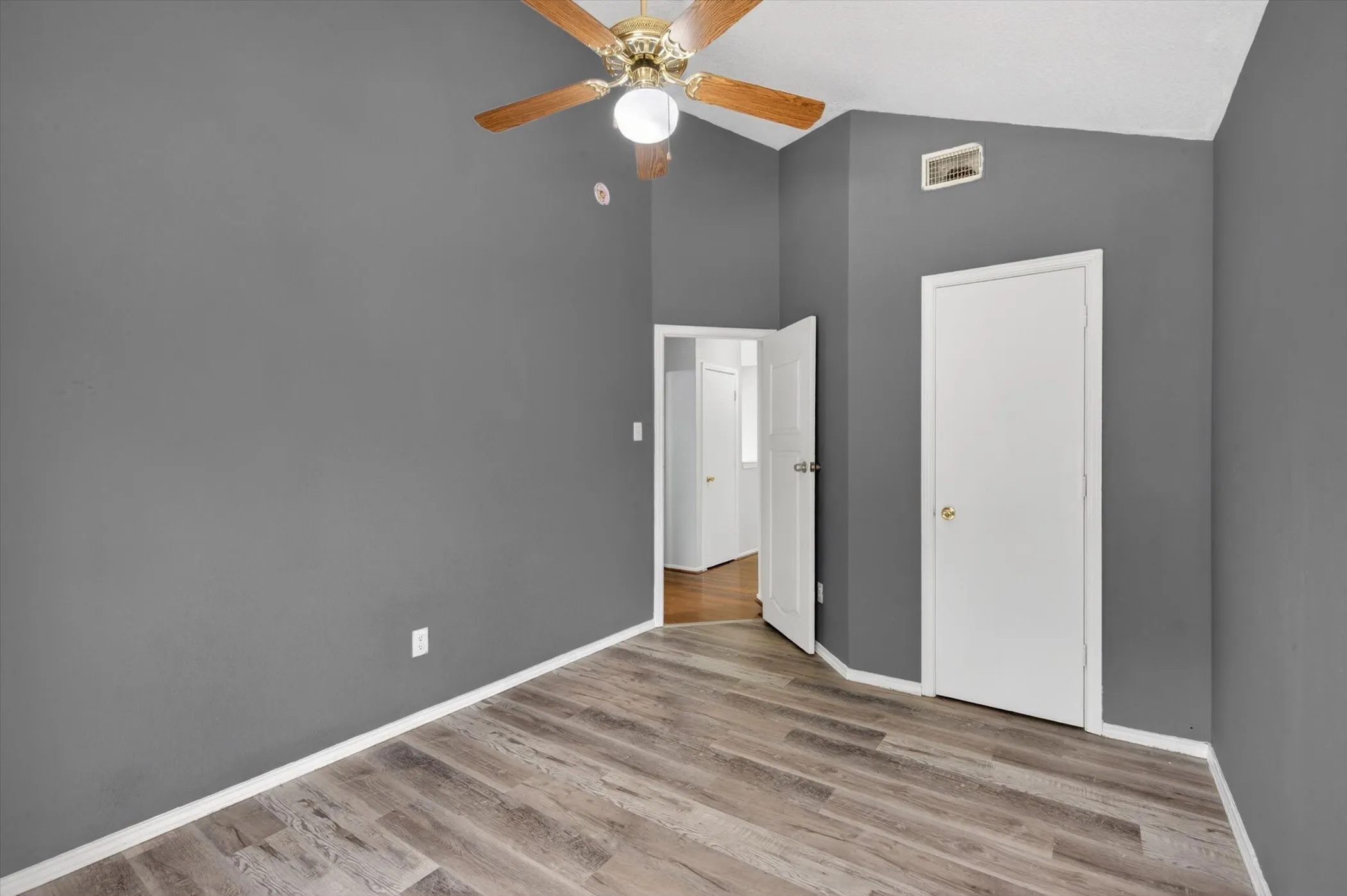 Vaulted ceiling room featuring wood-finish flooring, a ceiling fan with light fixture, and a neutral wall color