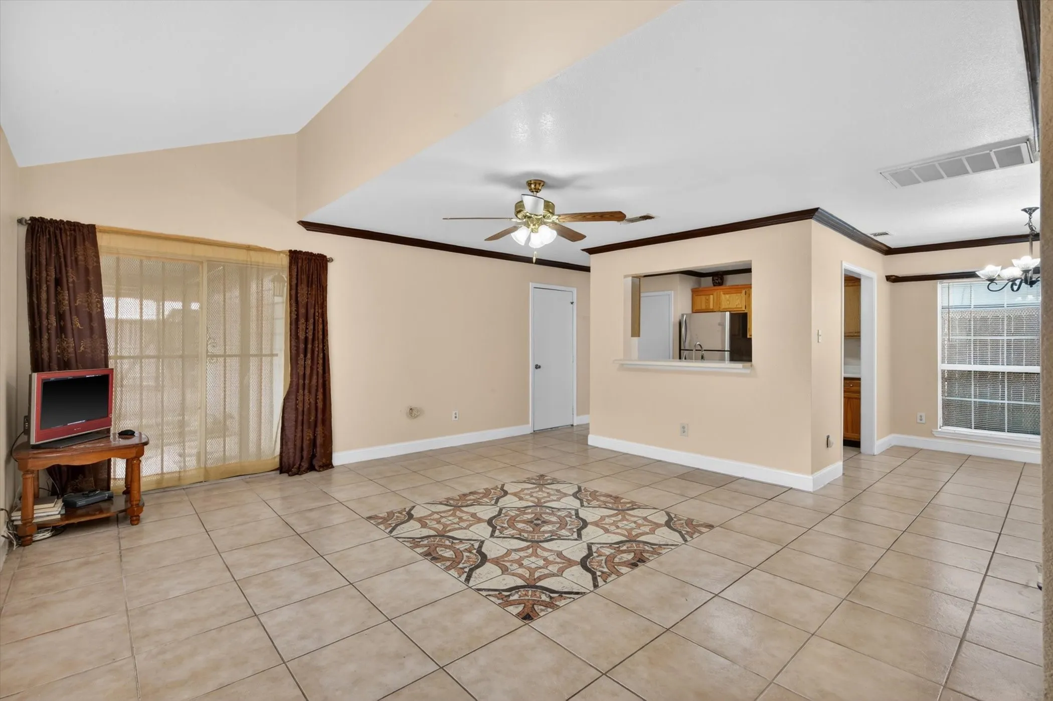 Spacious open-concept room featuring vaulted ceilings and tile flooring with a central decorative tile inlay