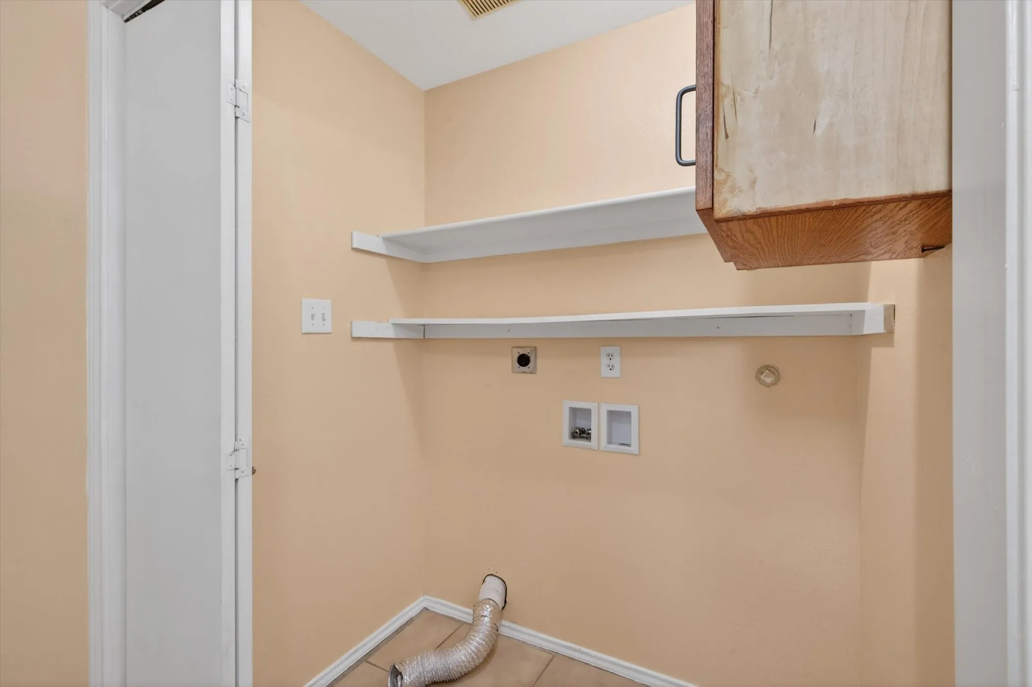 Utility area with two white wall shelves, a light wood-finish wall cabinet, and tile flooring