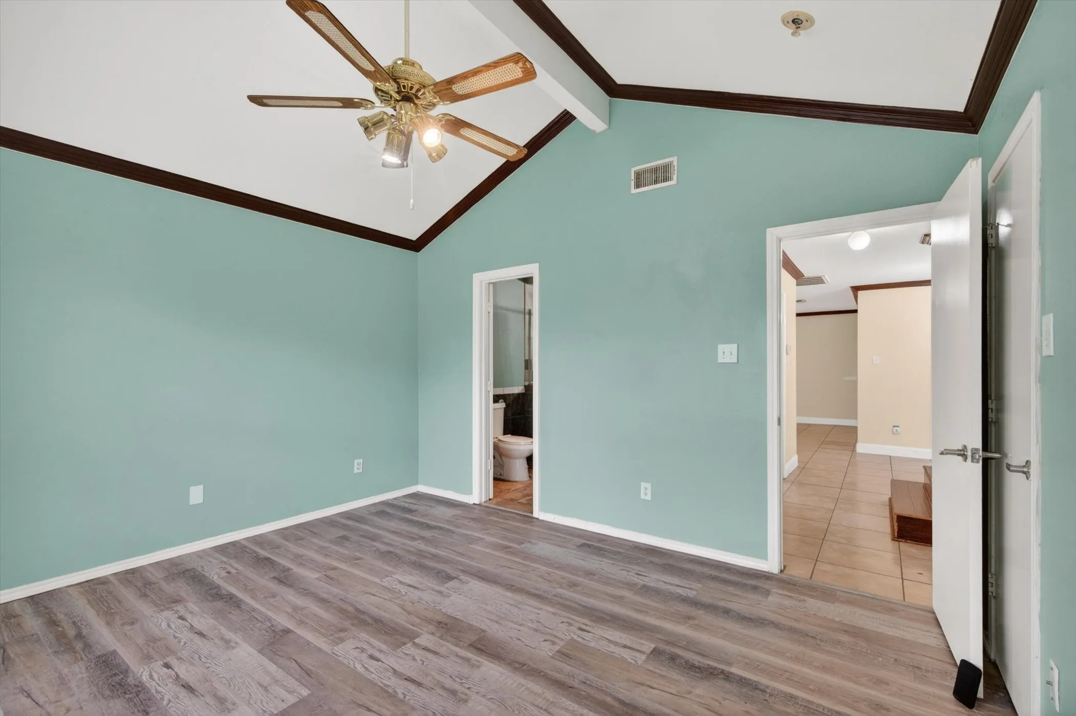 Vaulted ceiling bedroom featuring wood-finish flooring, a ceiling fan with integrated lighting, and a neutral wall color palette with dark trim