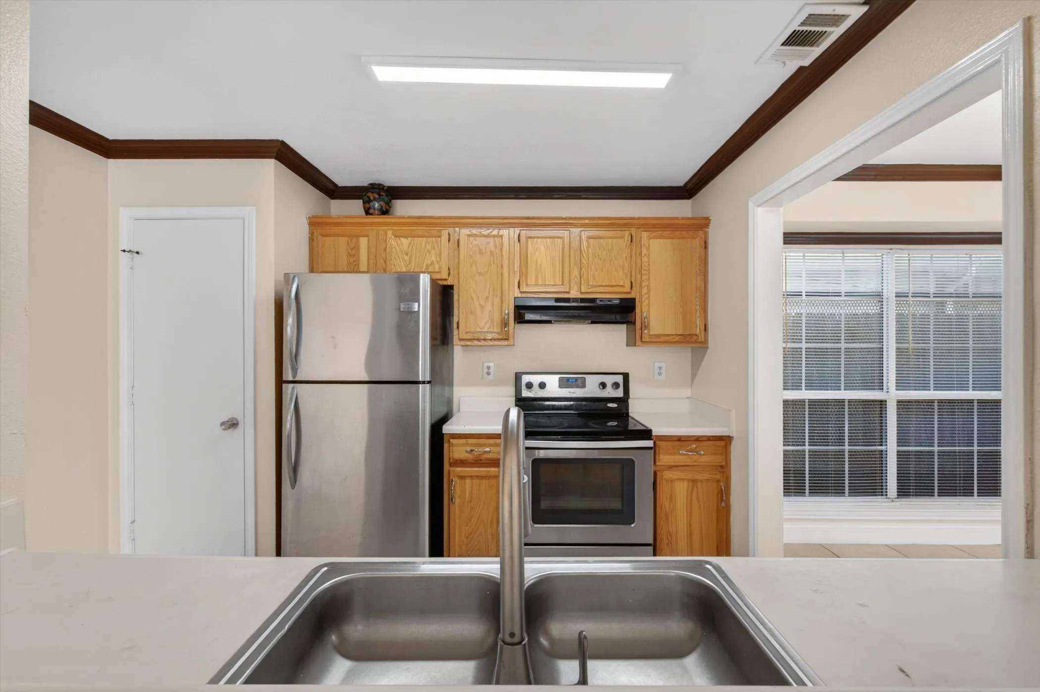 Kitchen featuring a stainless steel double-basin sink, light wood cabinetry, white countertops, and stainless steel appliances