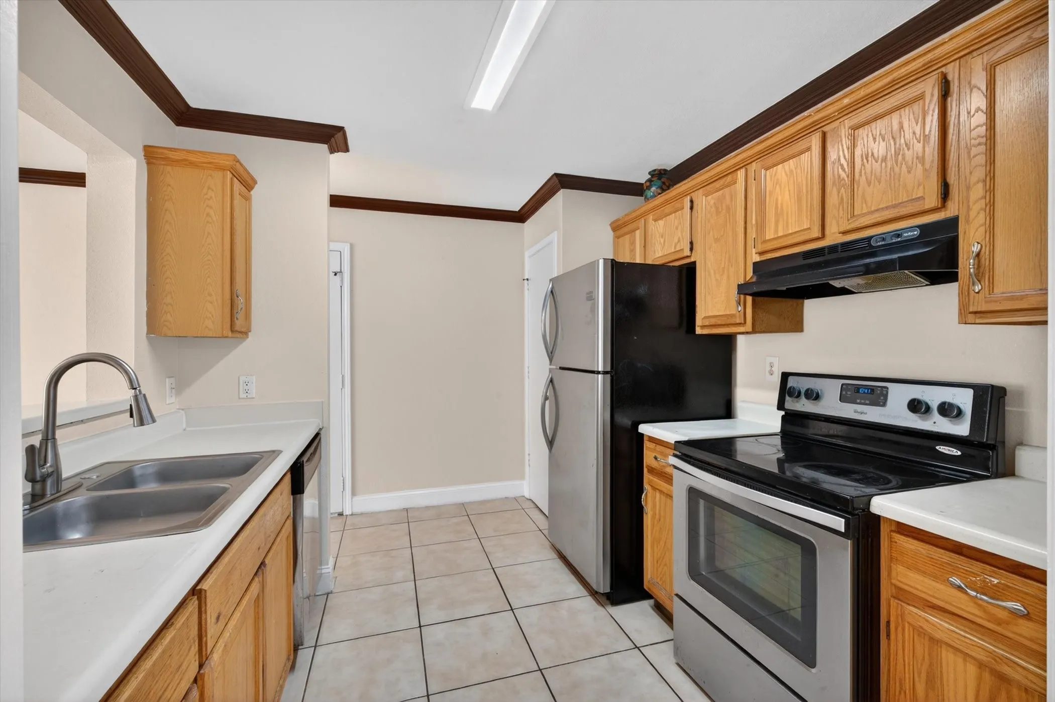 Kitchen featuring light wood cabinetry, light countertops, dual basin stainless steel sink with a gooseneck faucet, black and stainless steel appliances, and square floor tiling