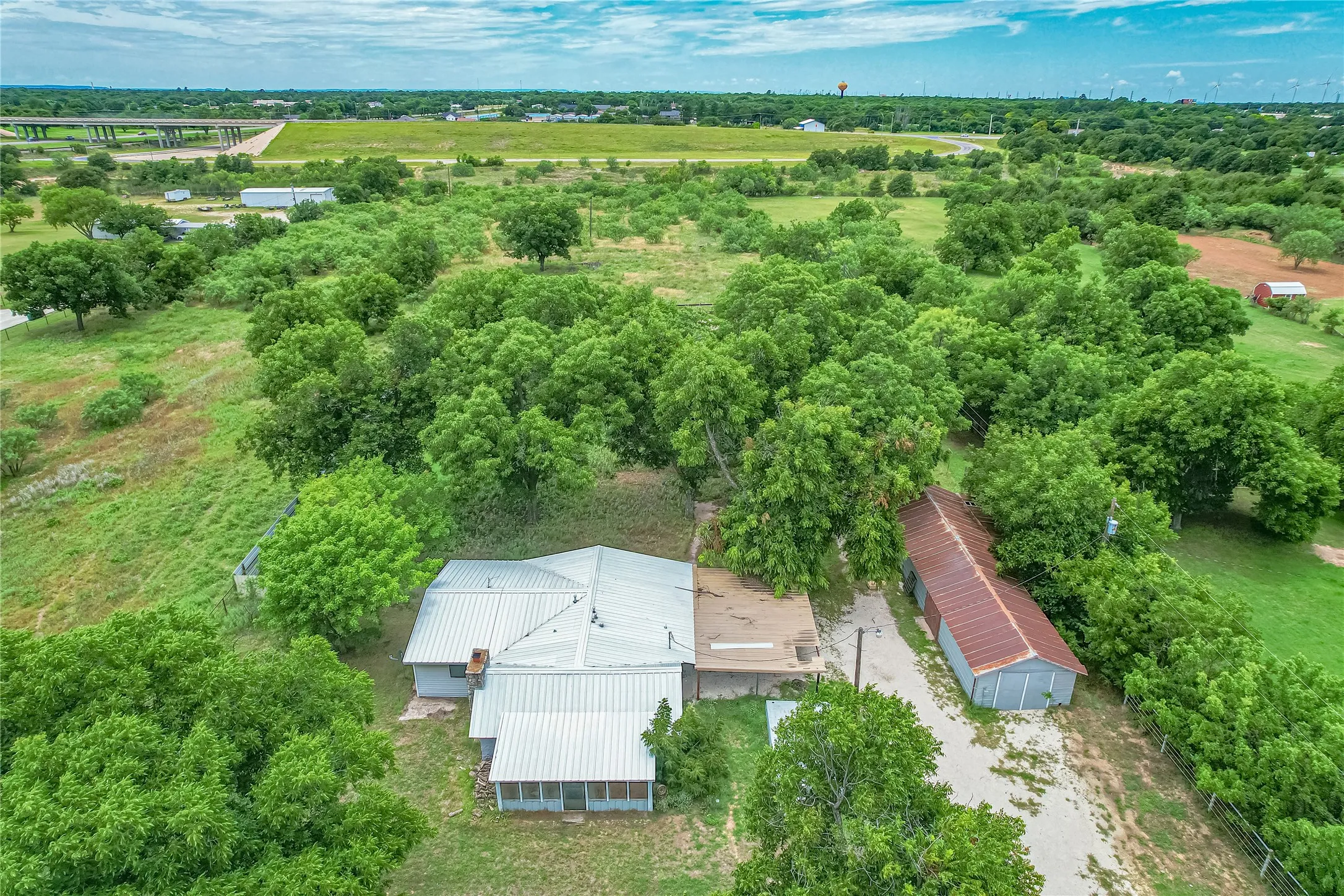 Expansive property featuring a single-story residence with a metal roof, a screened porch, and a detached outbuilding with a corrugated metal roof