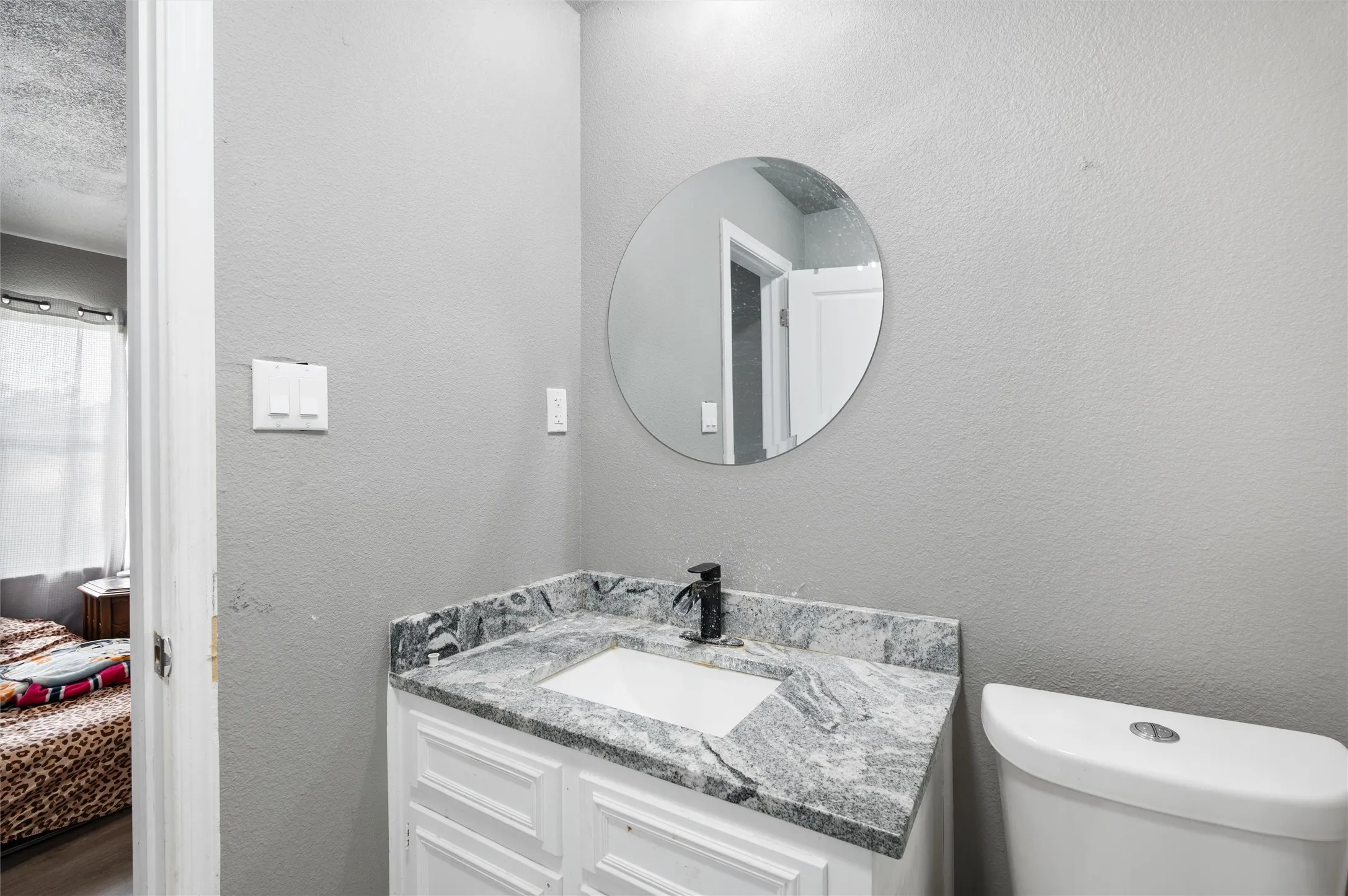 Bathroom featuring a white vanity with paneling, a patterned stone countertop, and an undermount sink with a matte black faucet
