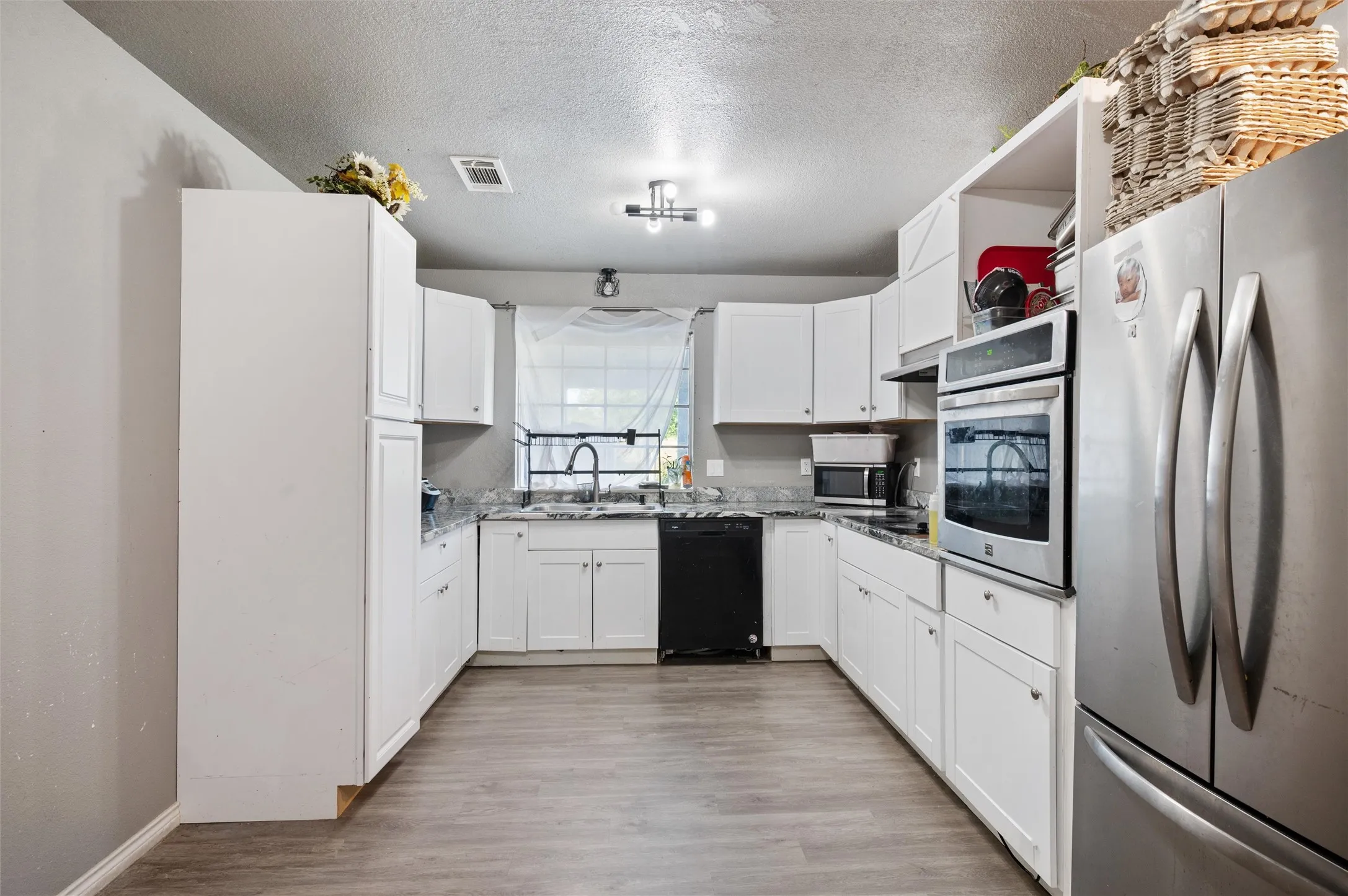 U-shaped kitchen featuring white cabinetry, grey wood-finish flooring, a stainless steel refrigerator, built-in stainless steel oven, and a black dishwasher