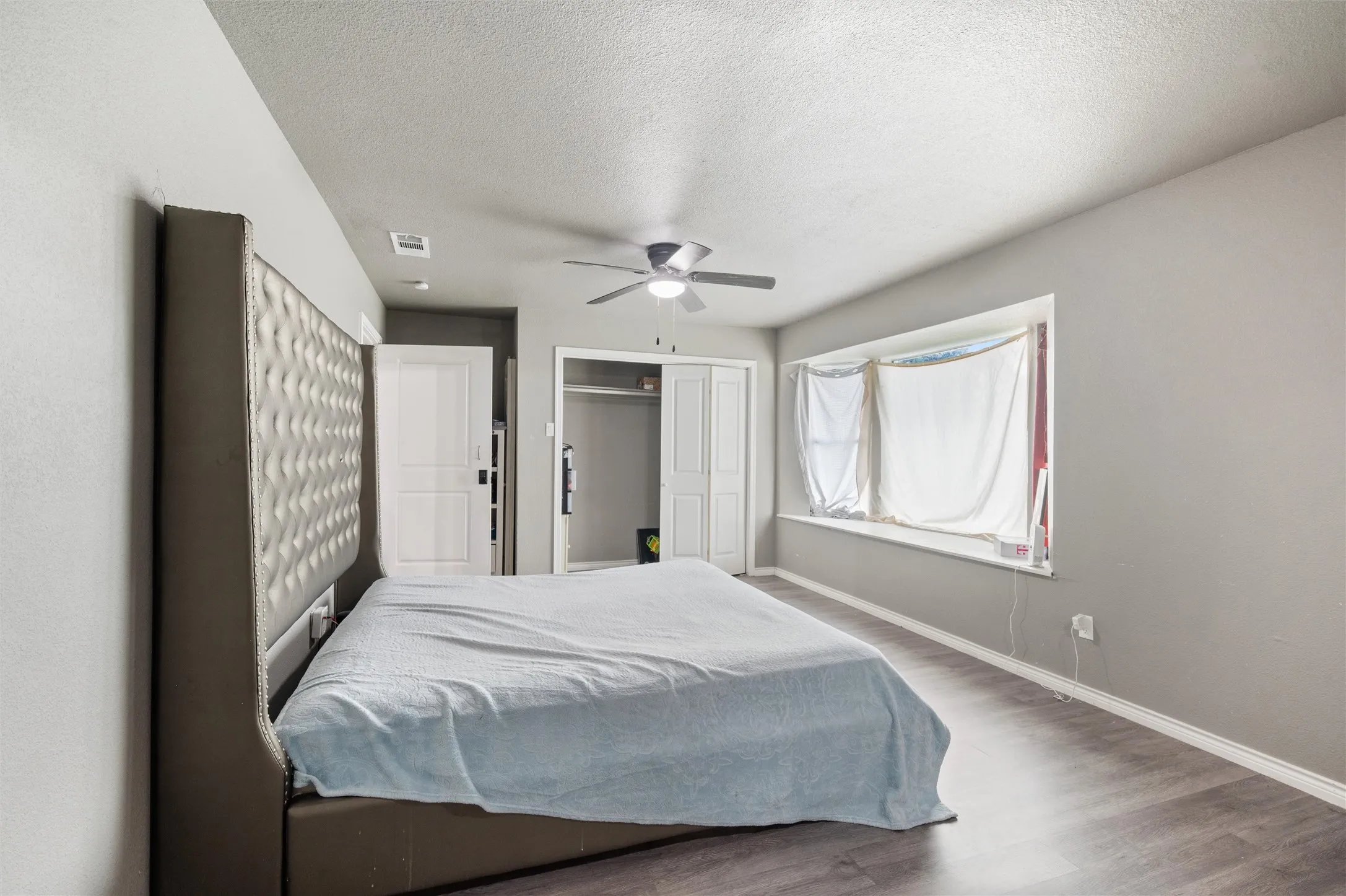 Spacious bedroom featuring wood-finish flooring, a contemporary ceiling fan, and ample natural light from a wide window