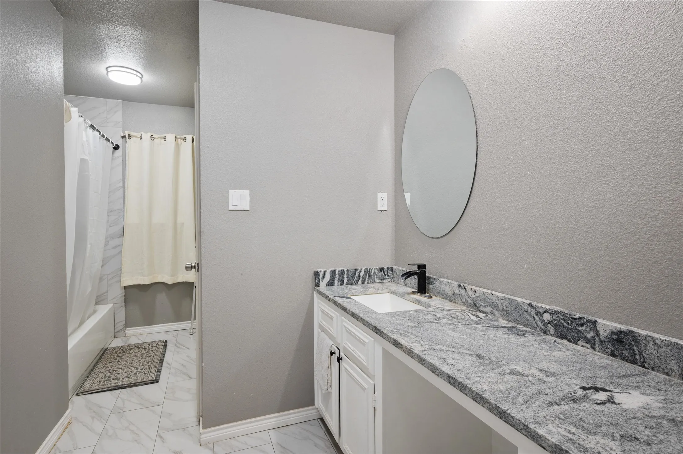 Bathroom featuring a wide vanity with a patterned countertop, integrated sink, and matte black faucet