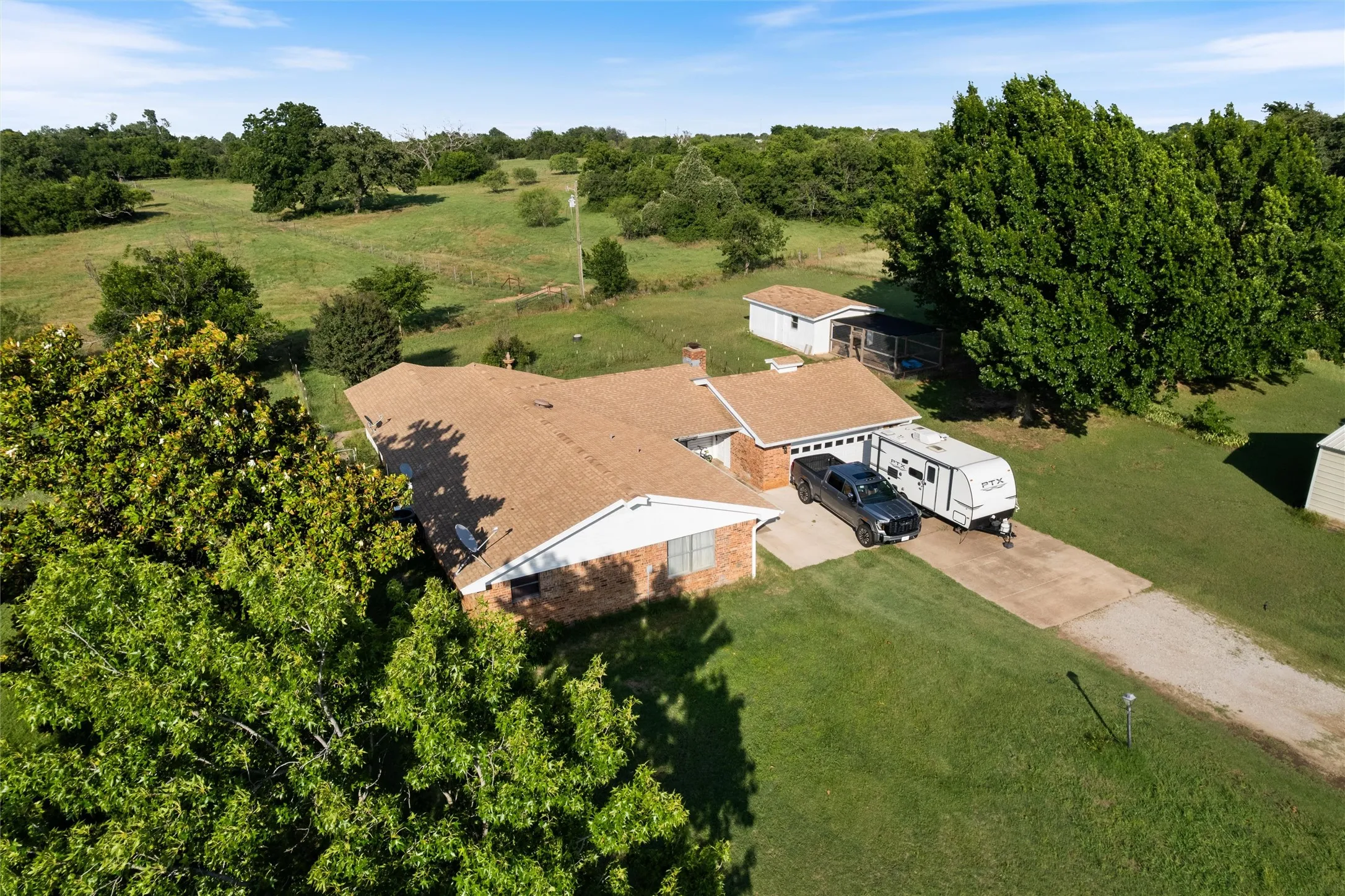 Brick exterior property featuring an attached two-car garage, extensive concrete driveway, and a secondary detached outbuilding