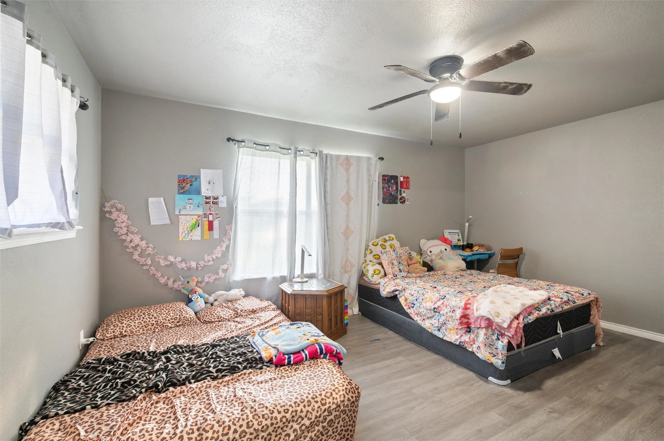 Room featuring wood-finish flooring, two windows with white blinds, and a ceiling fan with integrated lighting