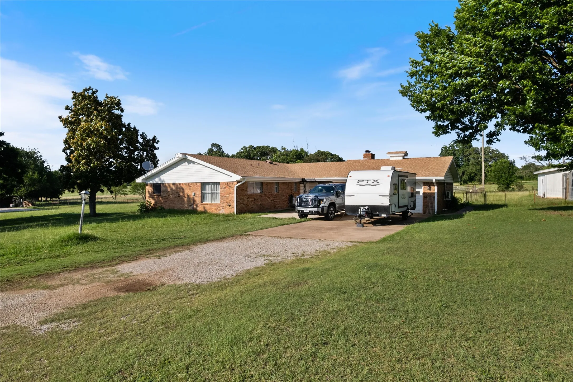 Brick ranch-style residence featuring a gravel driveway, mature trees, and an expansive lawn