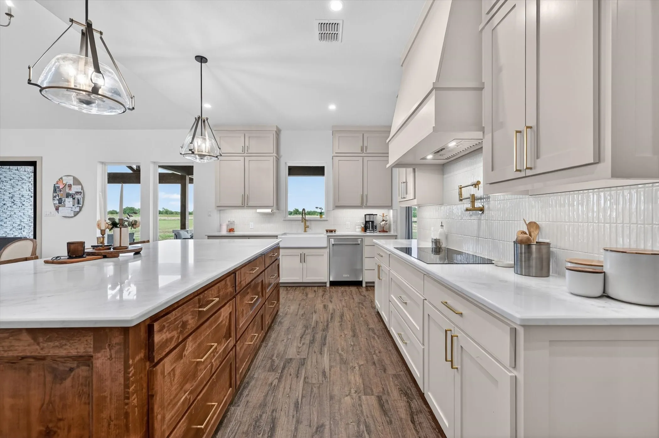 Gourmet kitchen featuring a large central island with wood cabinetry, light-biege perimeter cabinetru stone countertops, wood-tile flooring, and pendant lighting