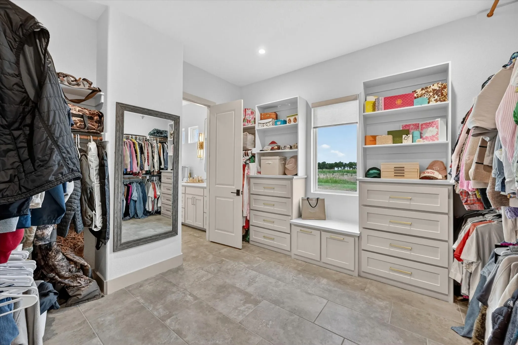 Spacious walk-in closet featuring extensive built-in cabinetry, integrated shelving, a full-length mirror, and tile flooring